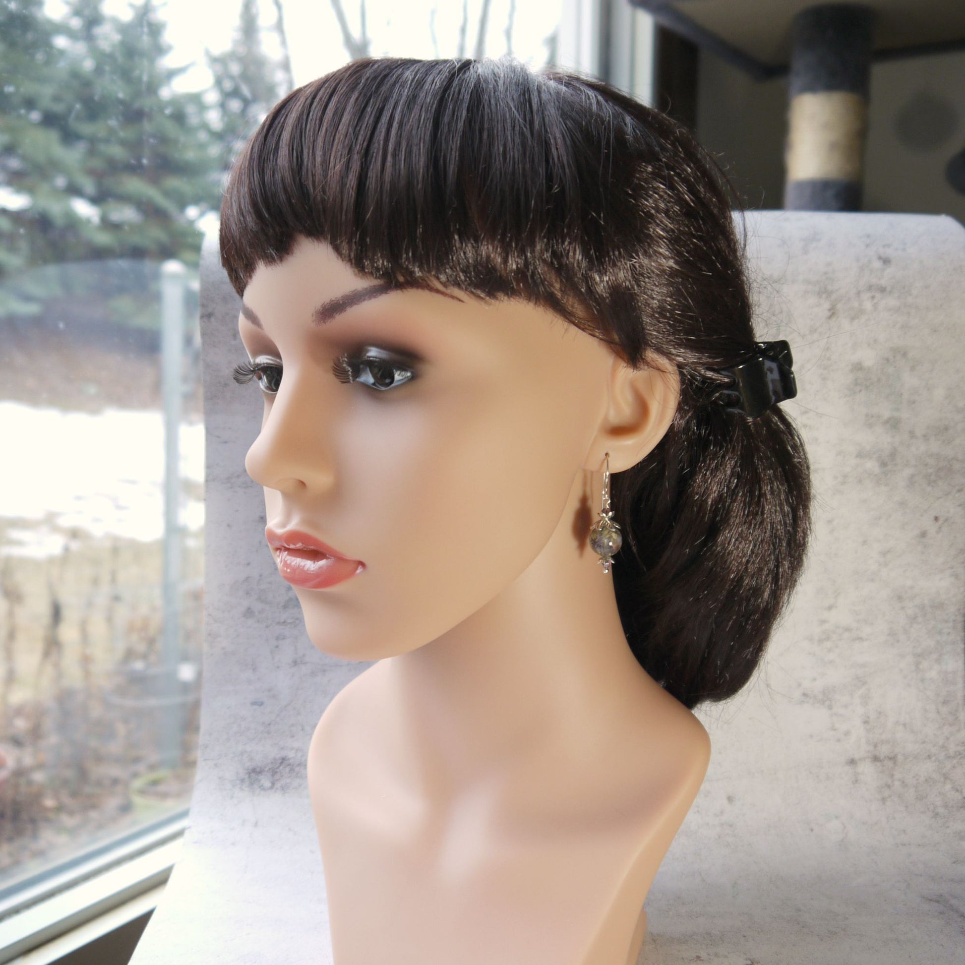 Mannequin head with a styled wig wearing real flower drop earrings on a blurred outdoor background