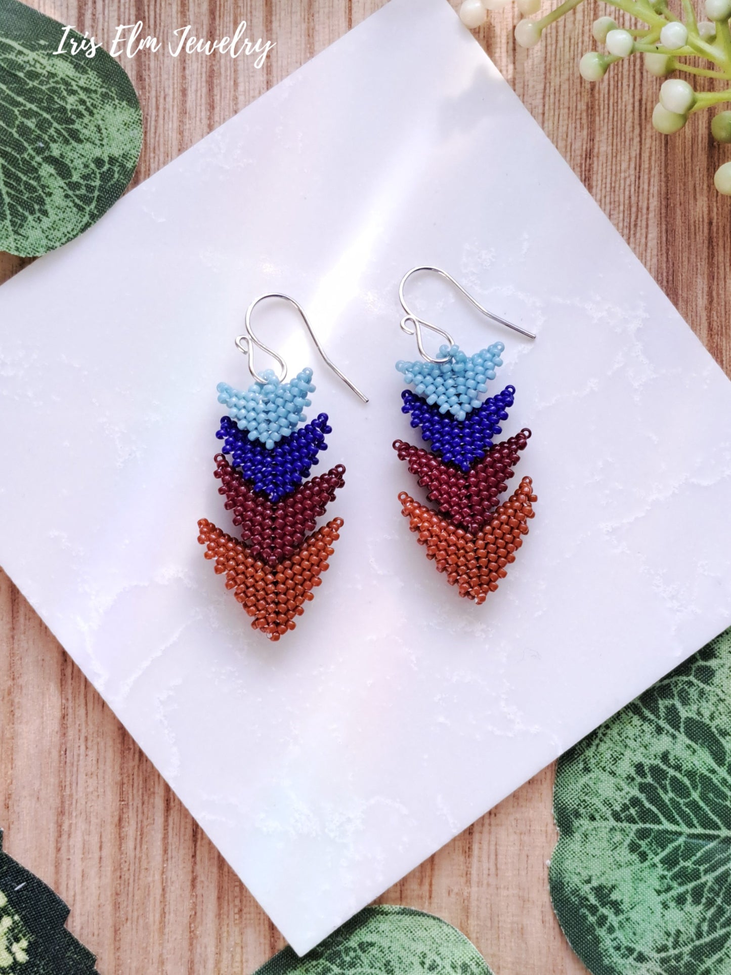 Colorful beaded seed bead beadwork triangle earrings on a white napkin with 'Iris Elm Jewelry' branding.