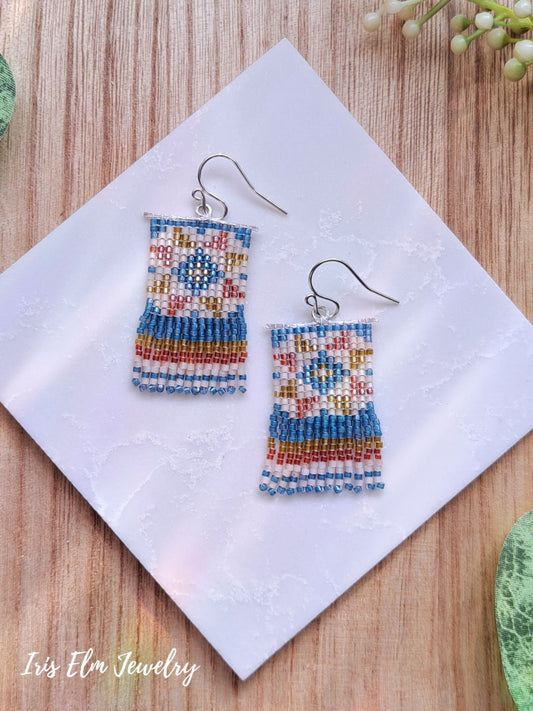 Colorful beaded quilt block seed bead fringe sterling silver earrings on a white napkin with 'Iris Elm Jewelry' branding.