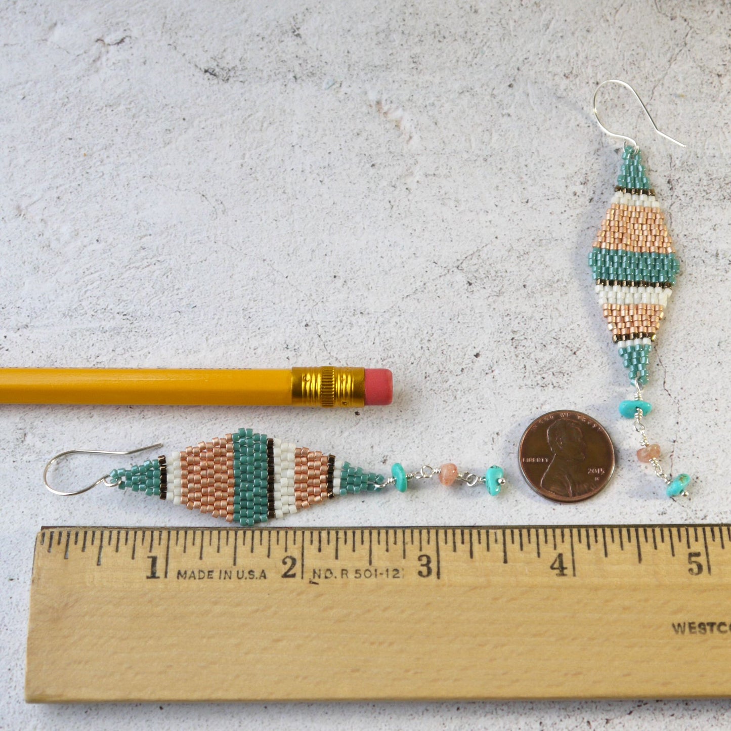 3.5 inch long Beaded earrings with a pencil and penny for scale on a light gray background