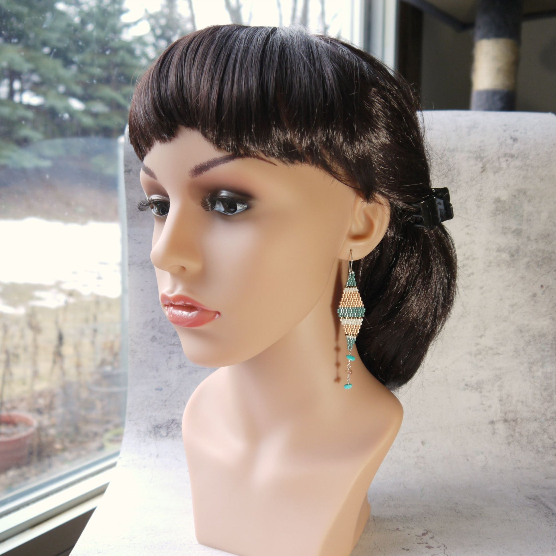 Mannequin head with a black wig and striped seed bead kite earrings in front of a window.