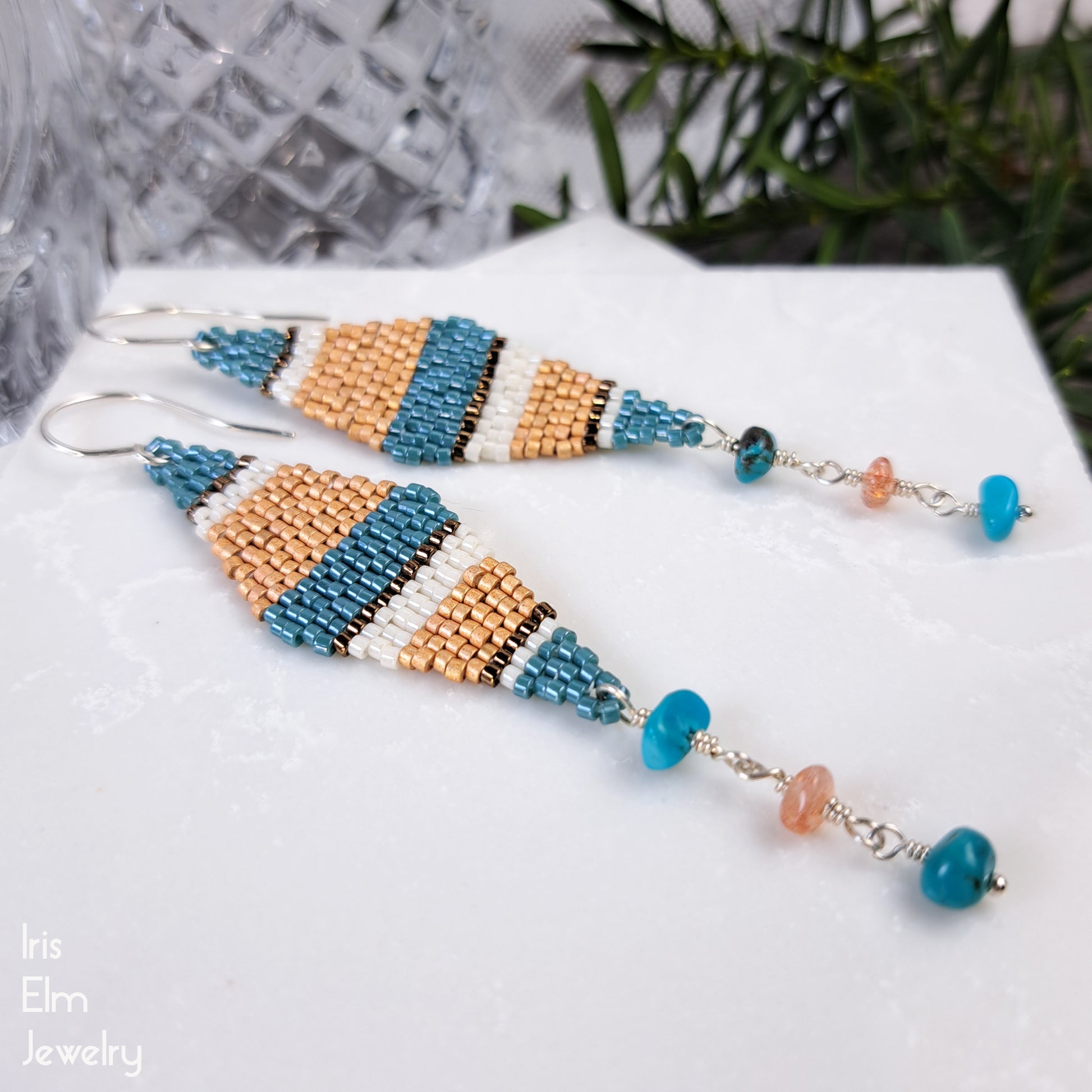 Beaded earrings with blue and orange stripes and turquoise and sunstone gemstone accents on a white surface.