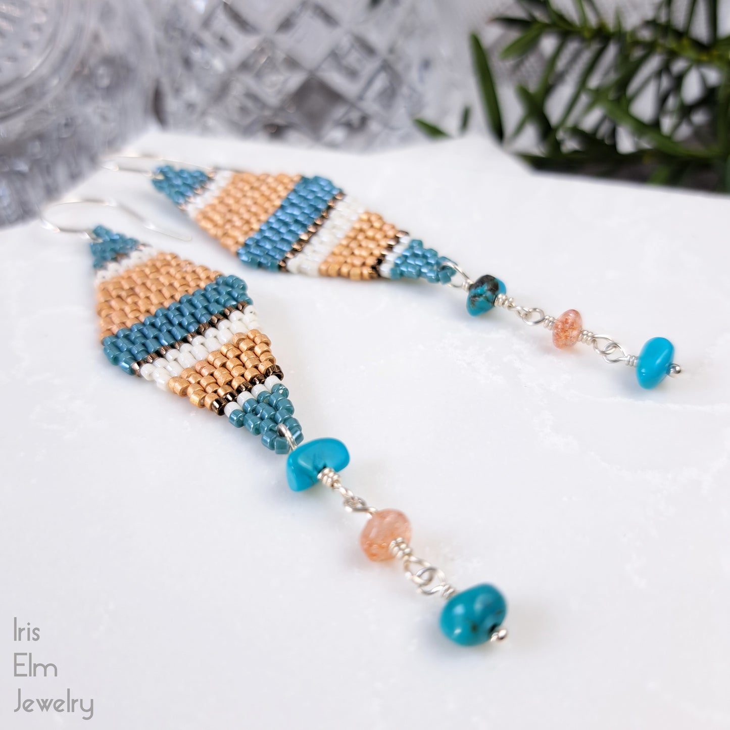 kite shaped beadwork seed bead earrings with blue and orange stripes with turquoise gemstone and sunstone dangling beneath on a white surface