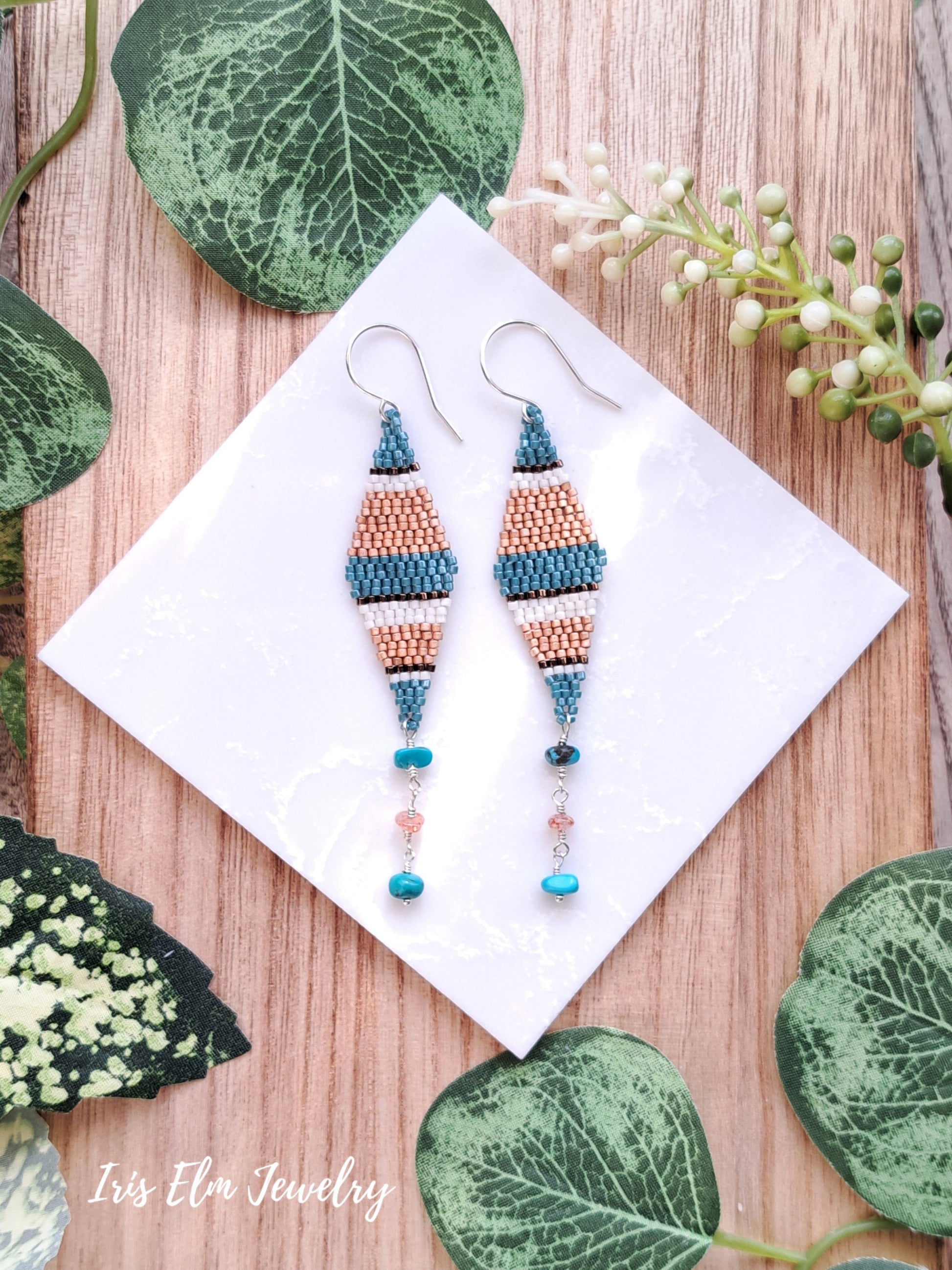 Pair of beaded turquoise and sunstone seed bead diamond kite earrings on a white card with green leaves in the background