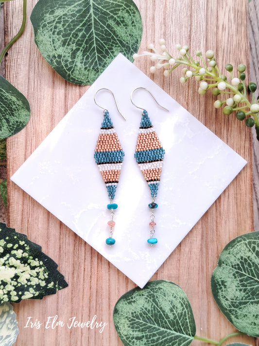 Pair of beaded turquoise and sunstone seed bead diamond kite earrings on a white card with green leaves in the background