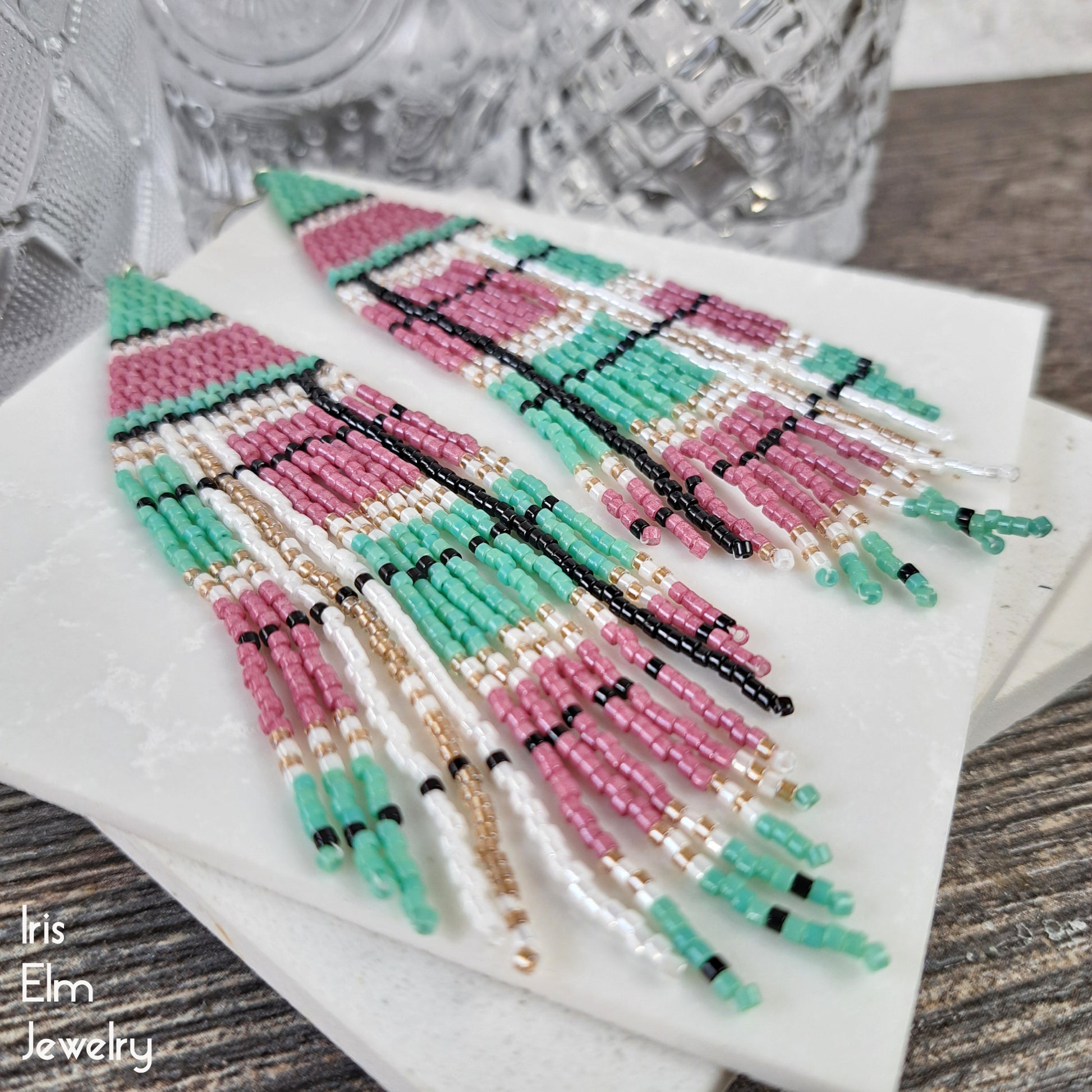 Beadwork long fringe earrings with pink and green plaid patterns on a white surface.