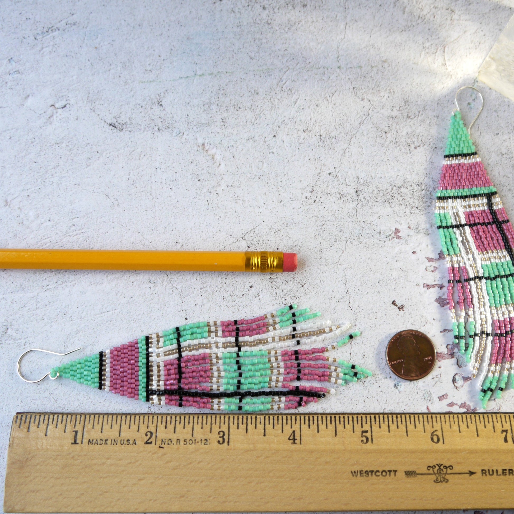 5 inch long pink and green plaid fringe seed bead fringe earrings next to a pencil and coin on a textured surface with a ruler for scale.