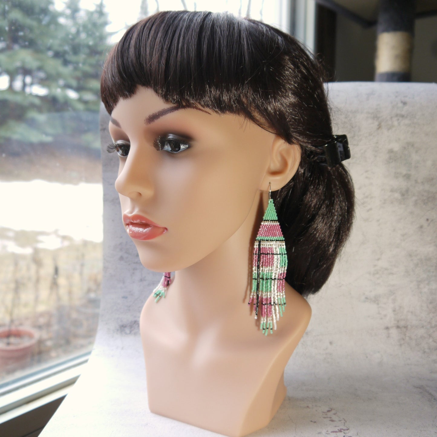 Mannequin head with a wig and colorful long fringe plaid earrings on a blurred background