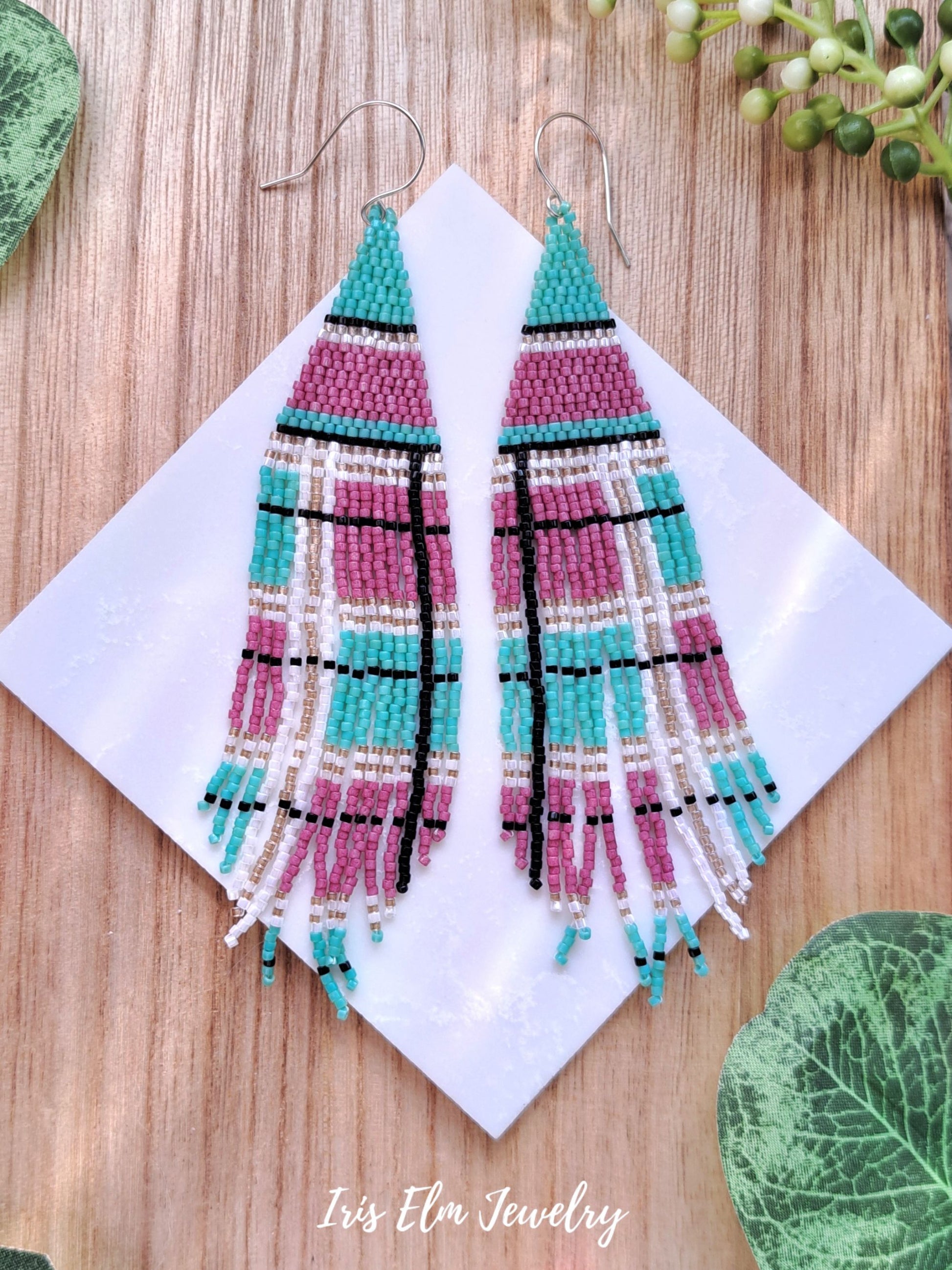 Colorful beaded pink and mint green plaid seed bead fringe earrings on a white card with 'Iris Elm Jewelry' branding, placed on a wooden surface.