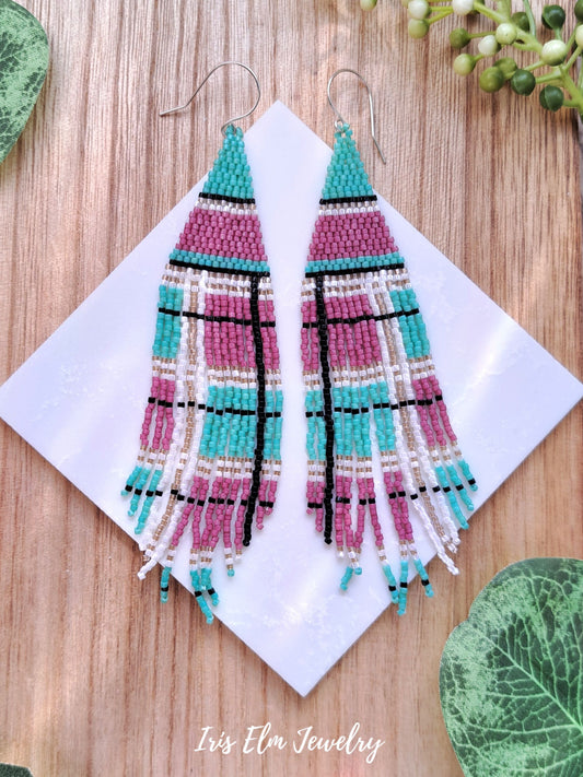 Colorful beaded pink and mint green plaid seed bead fringe earrings on a white card with 'Iris Elm Jewelry' branding, placed on a wooden surface.