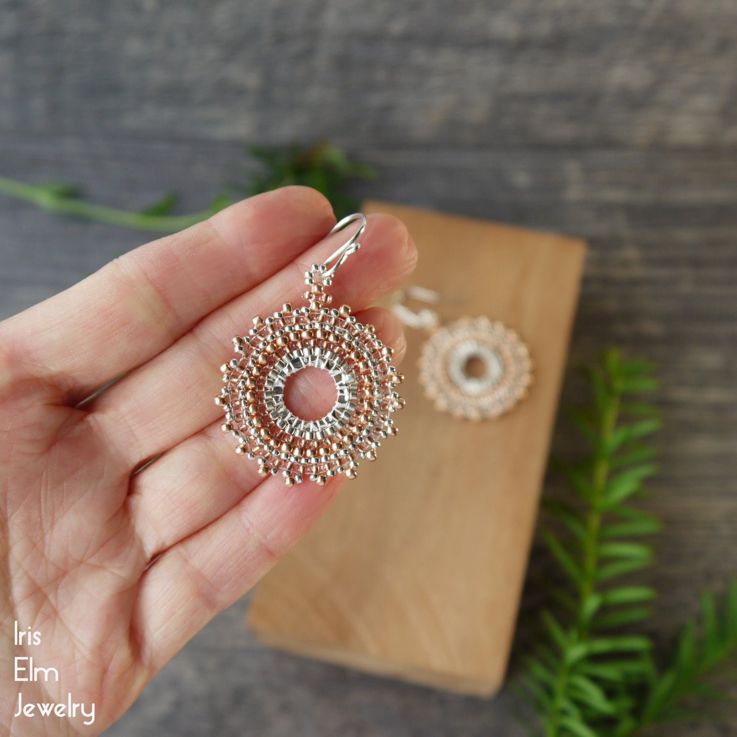 Decorative copper seed bead hoop earrings held in a hand with a blurred background