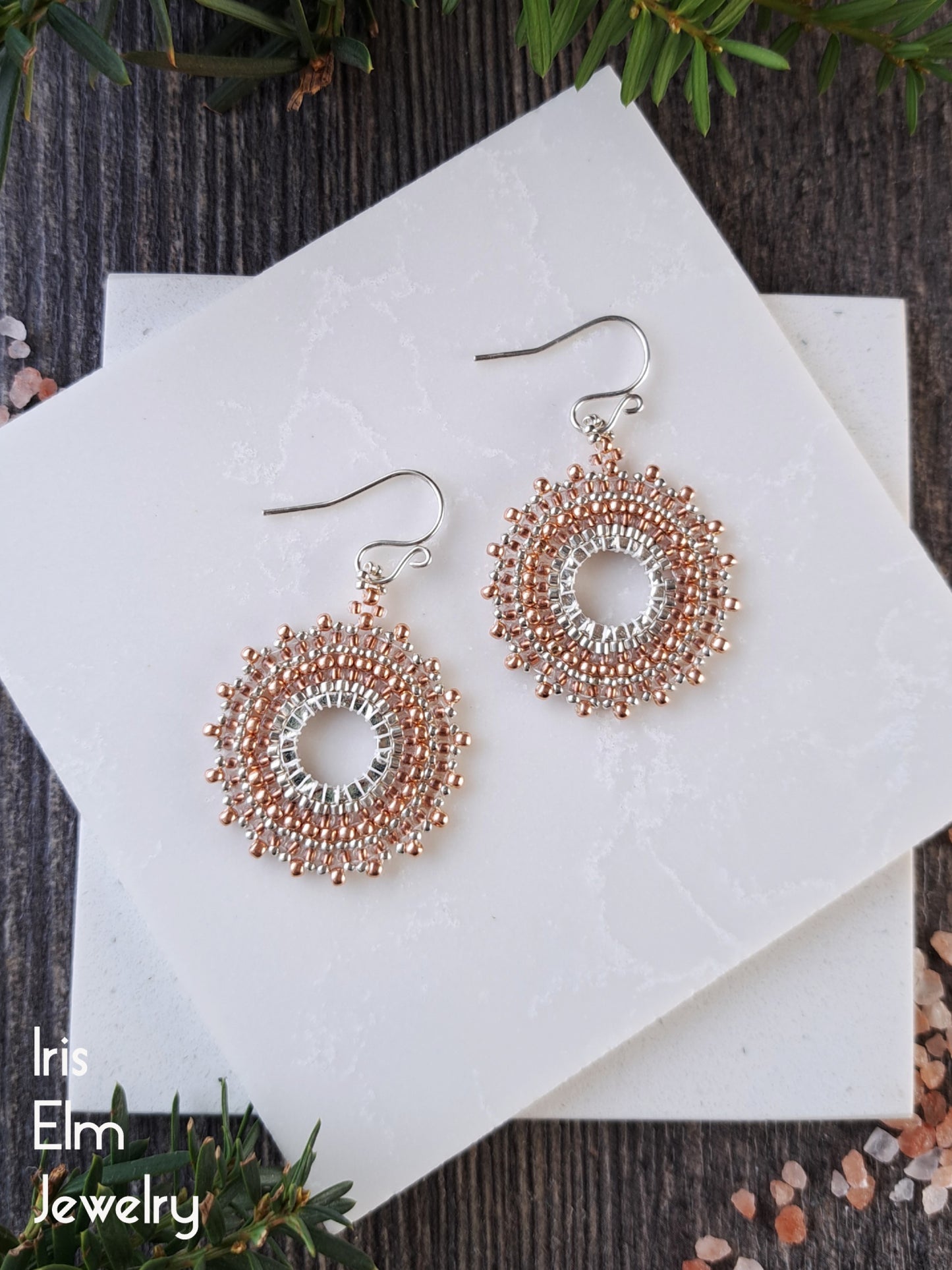 Pair of bright copper and silver woven hoop earrings on a white card with 'Iris Elm Jewelry' branding.