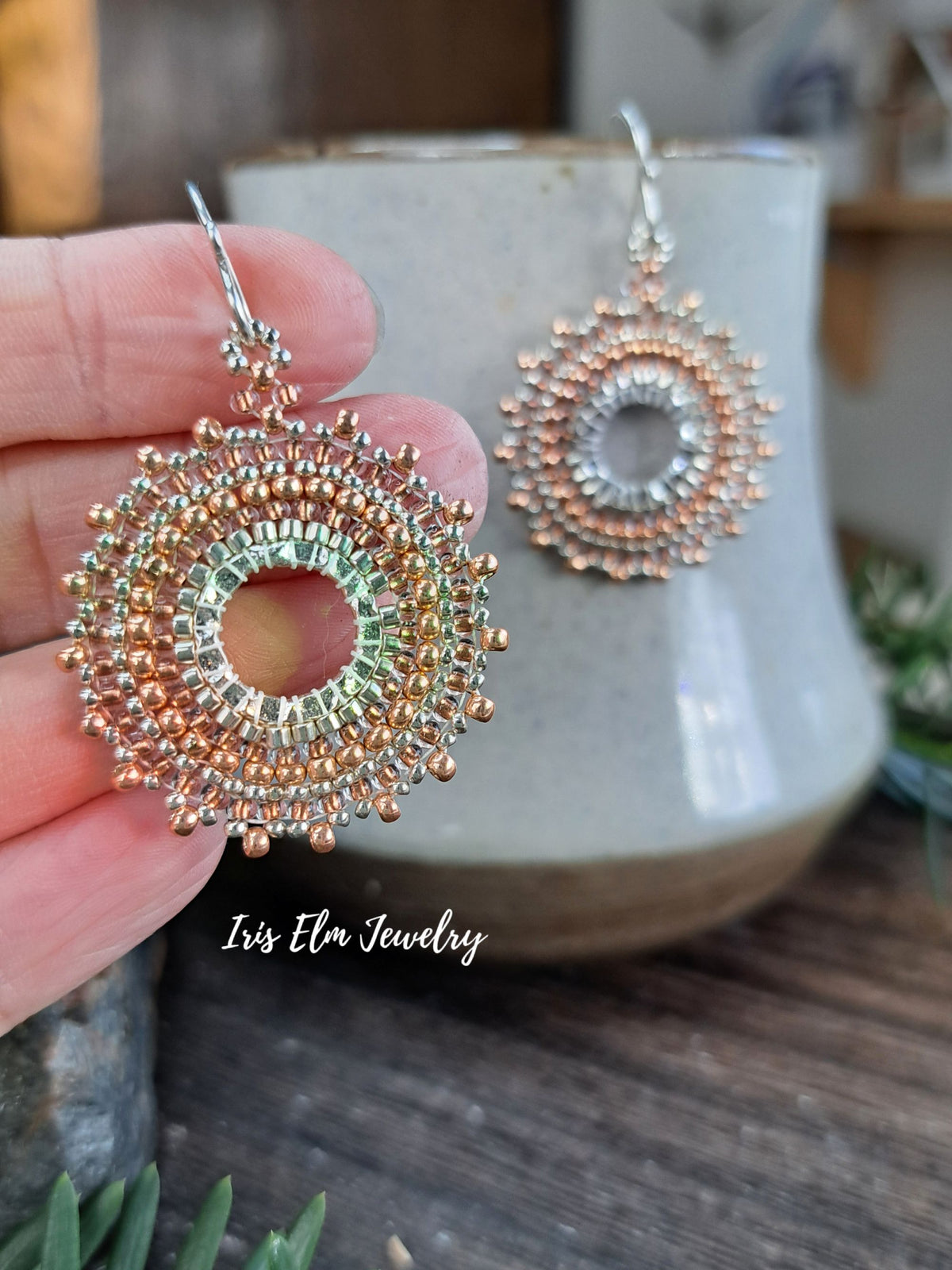 a pair of handmade beadwork circular hoop earrings woven with silver and copper colored glass seed beads by Iris Elm Jewelry  held in hand