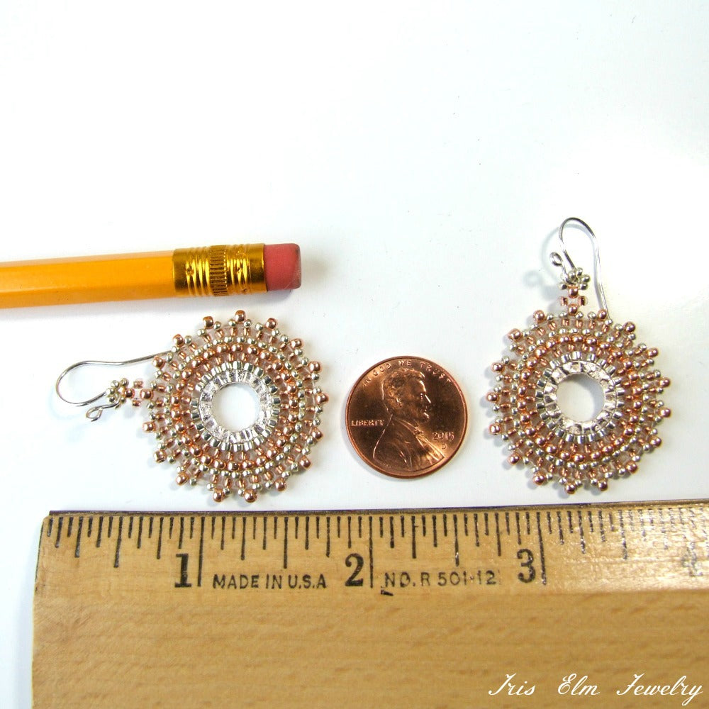 Two copper and silver earrings next to a penny and a ruler on a white background