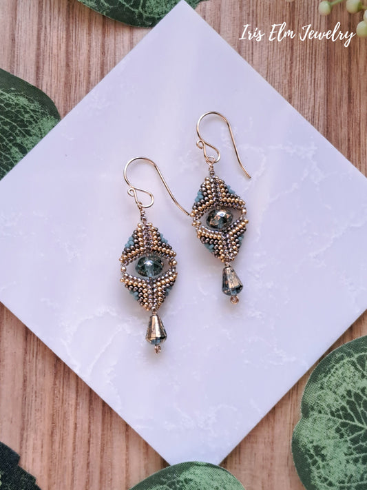 Pair of beaded aqua and gold glass beadwork art deco earrings on a white square with green leaves in the background