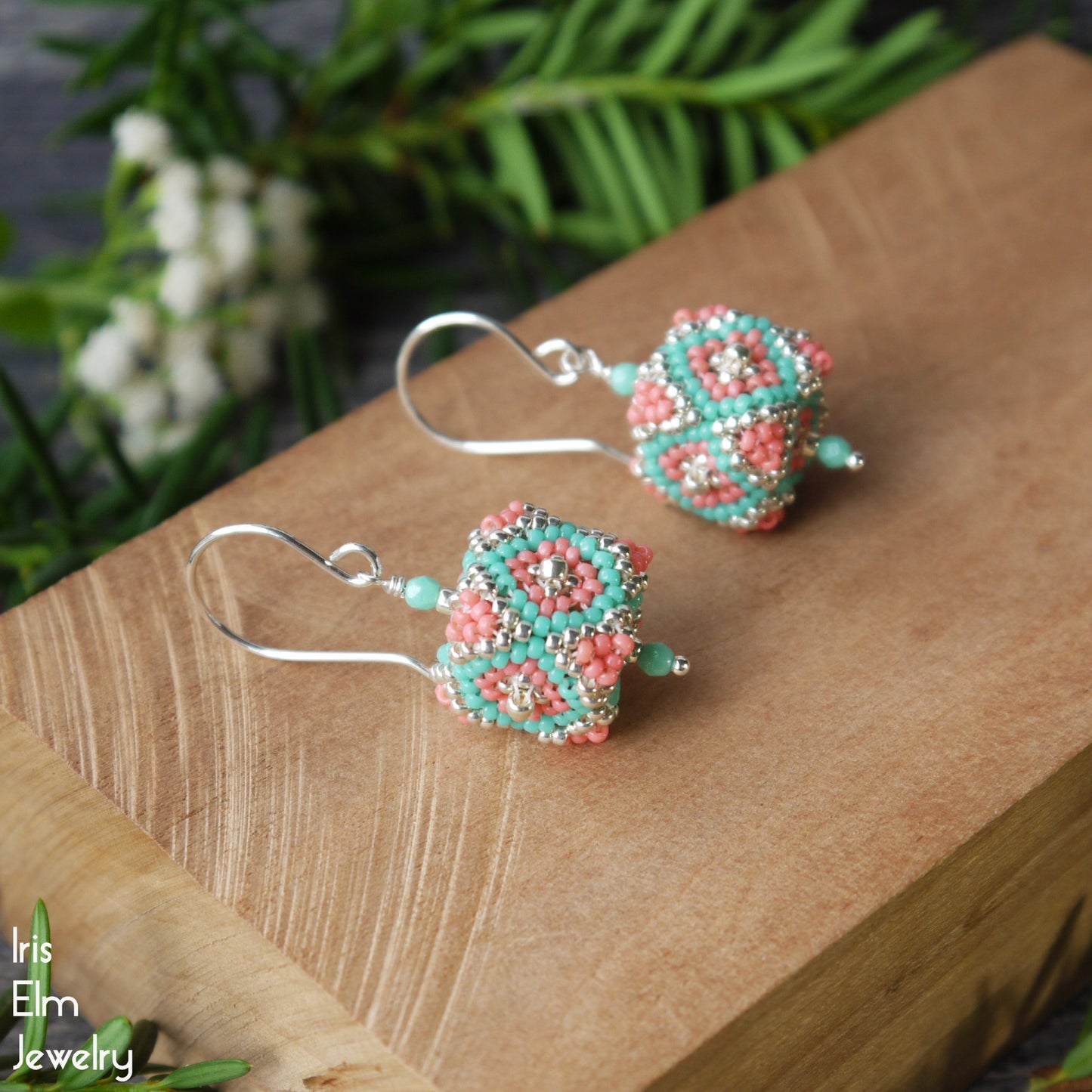 Beaded seed bead cube coral, silver, and turquoise glass earrings on a wooden surface with a natural background