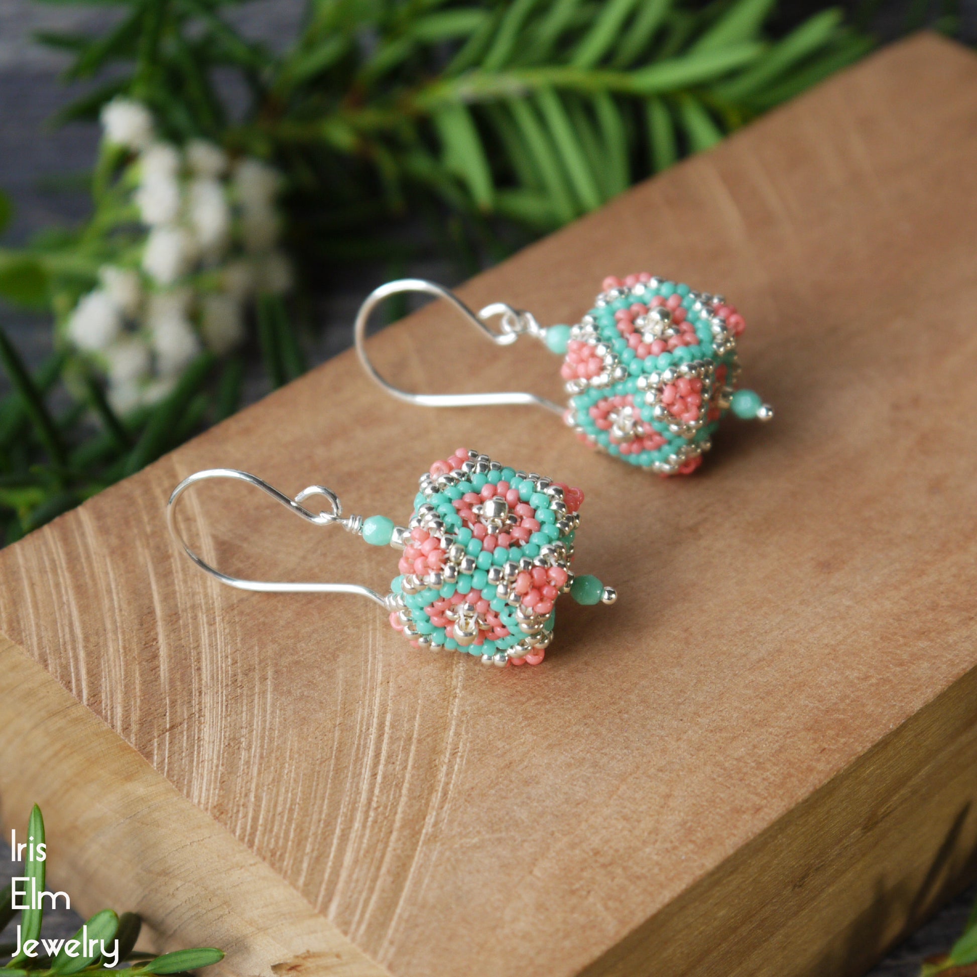 Beaded seed bead cube coral, silver, and turquoise glass earrings on a wooden surface with a natural background