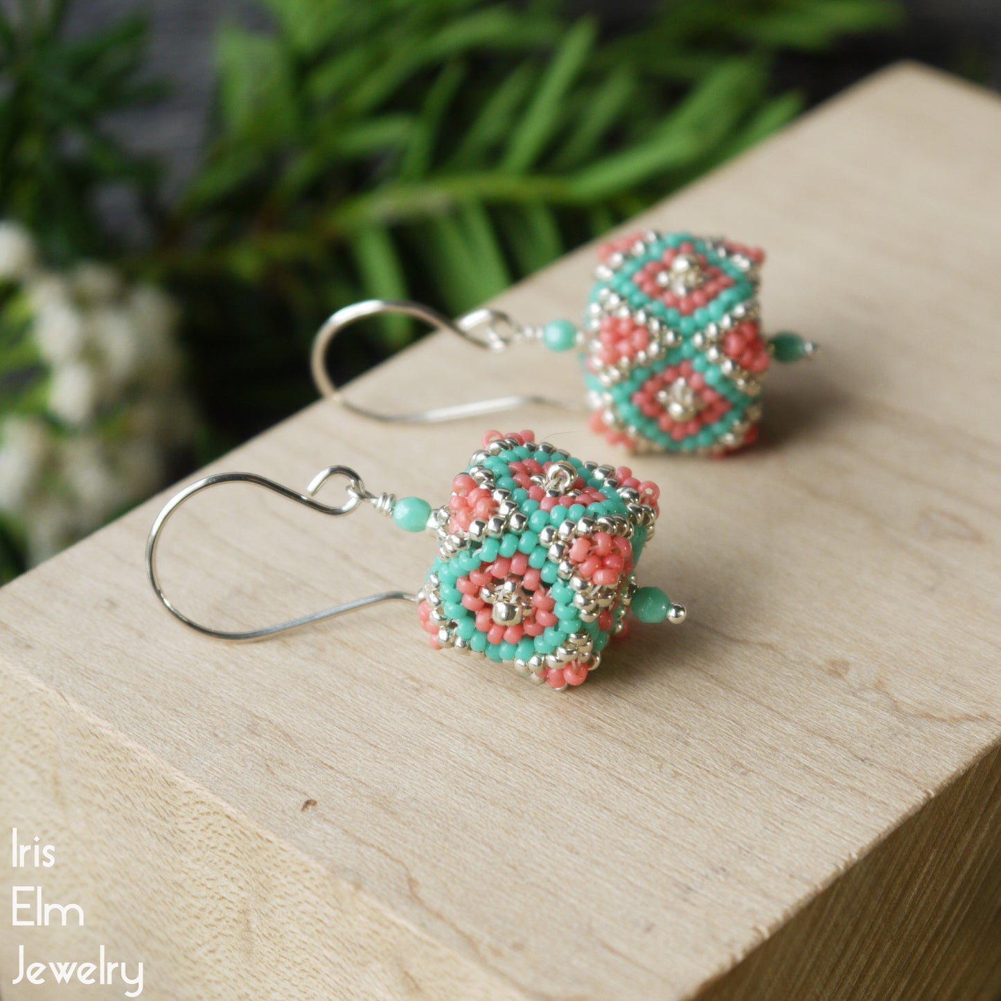 sterling silver handmade glass seed bead cube earrings on a wooden block with a natural background