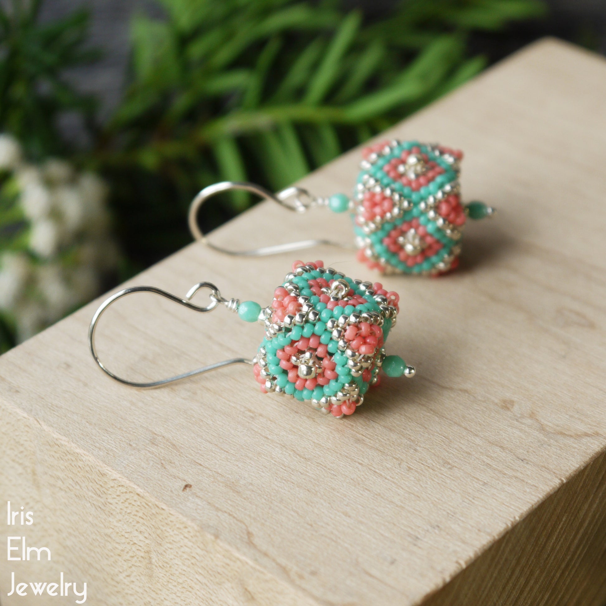 sterling silver handmade glass seed bead cube earrings on a wooden block with a natural background