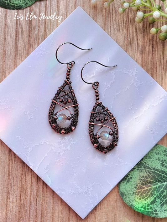 Pair of decorative copper wire woven viking labradorite earrings on a white square with 'Iris Elm Jewelry' branding.