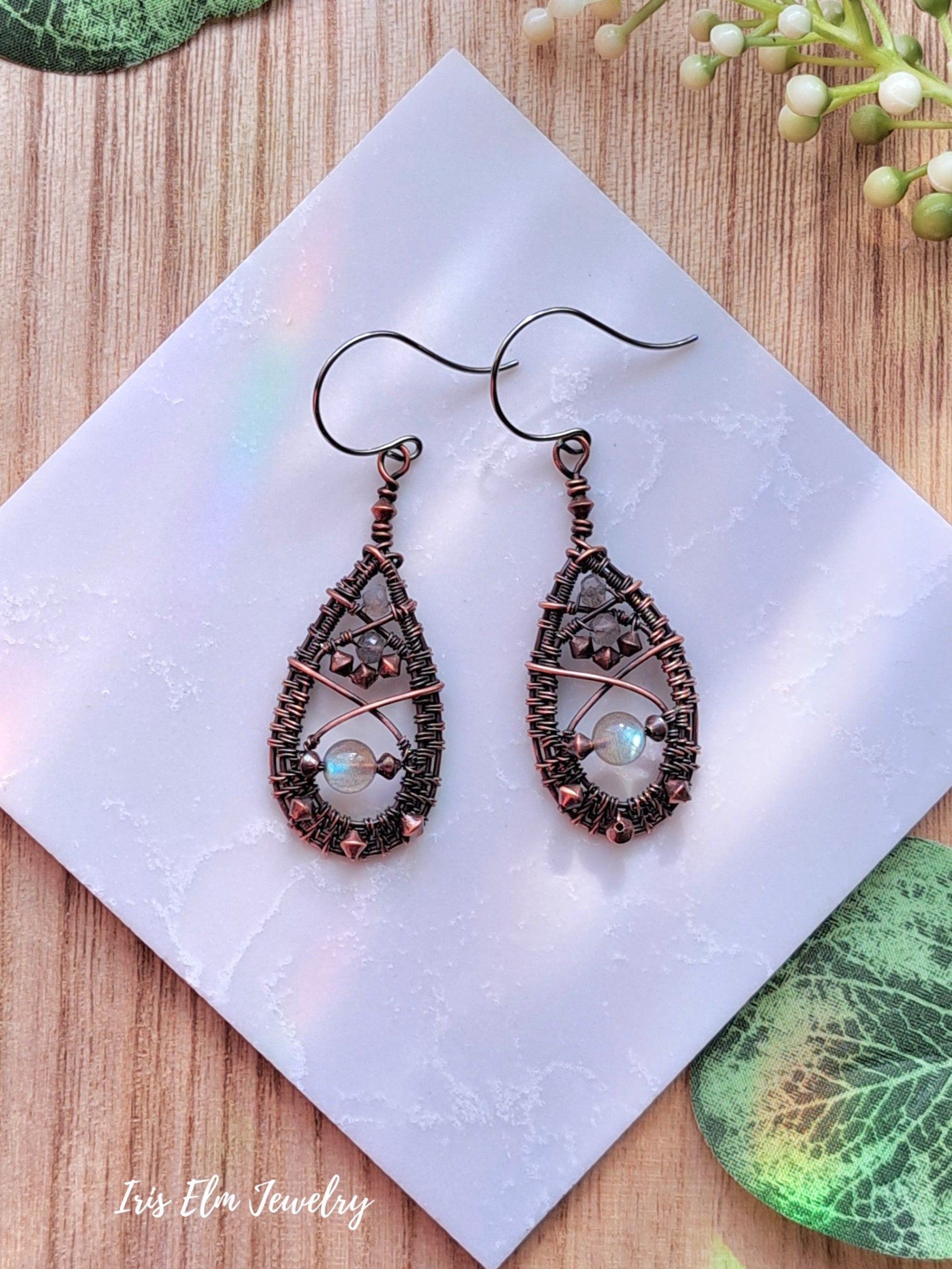 Pair of ornate labradorite copper wire wrapped teardrop earrings on a white napkin with 'Iris Elm Jewelry' branding.