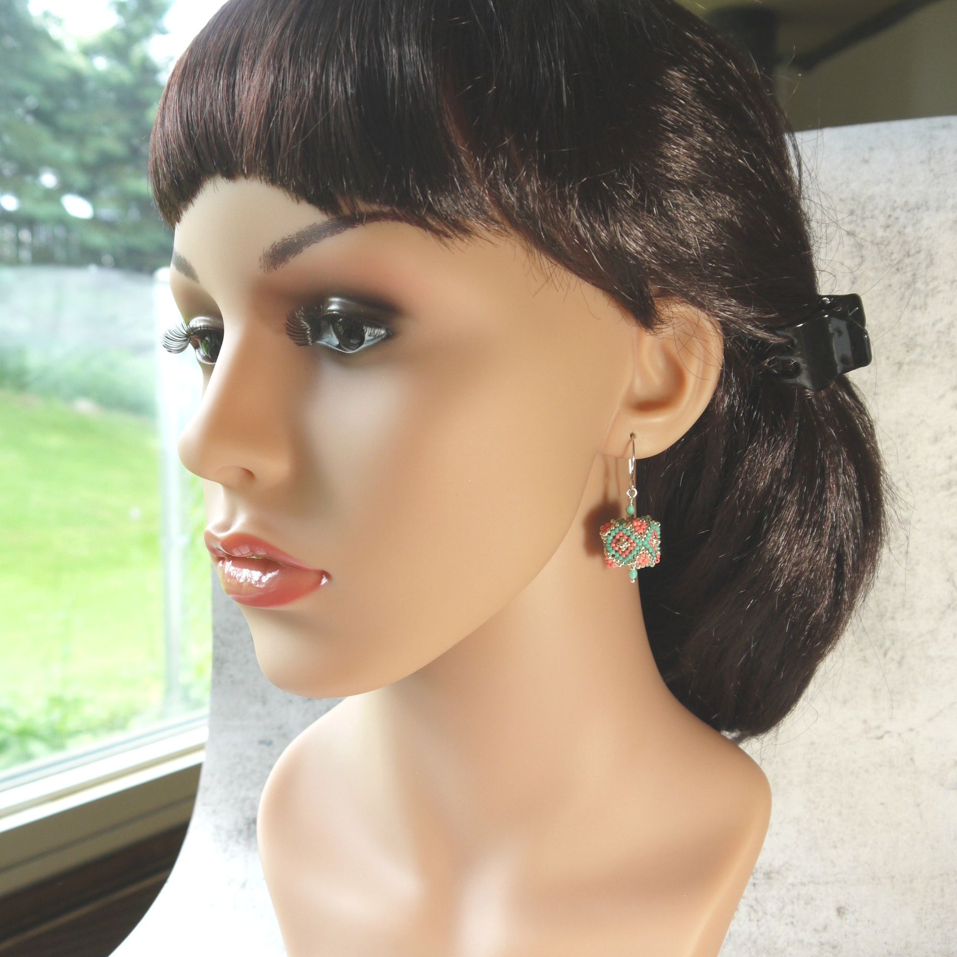 Mannequin head with dark hair and cube beaded earrings in front of a window