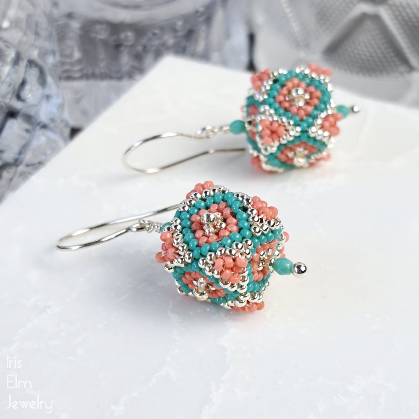 Pair of beaded sterling silver seed bead glass earrings with turquoise and coral colors on a white surface.