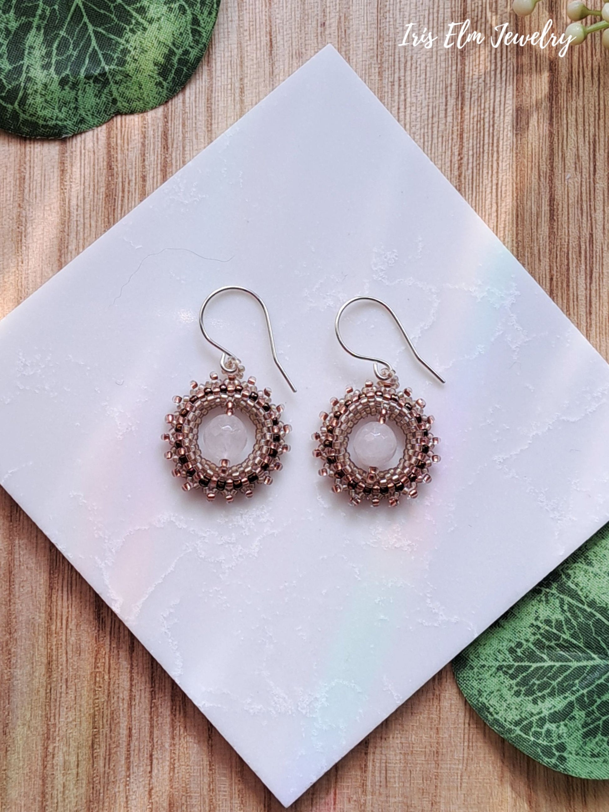 Pair of beadwork handmade rose quartz earrings on a white square with green leaves in the background