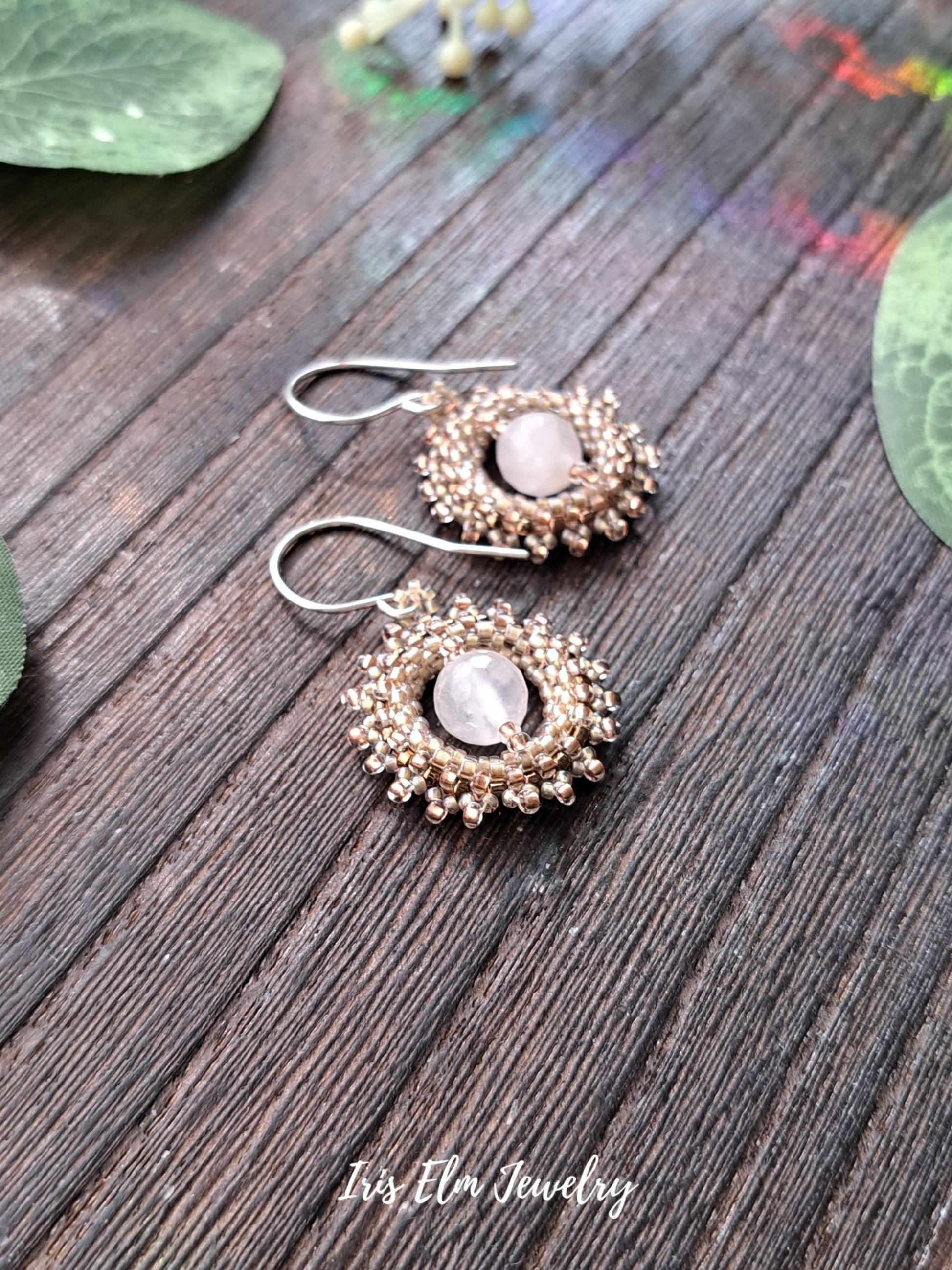 Pair of gold and pale pink rose quartz earrings on a wooden surface with 'Iris Elm Jewelry' branding.