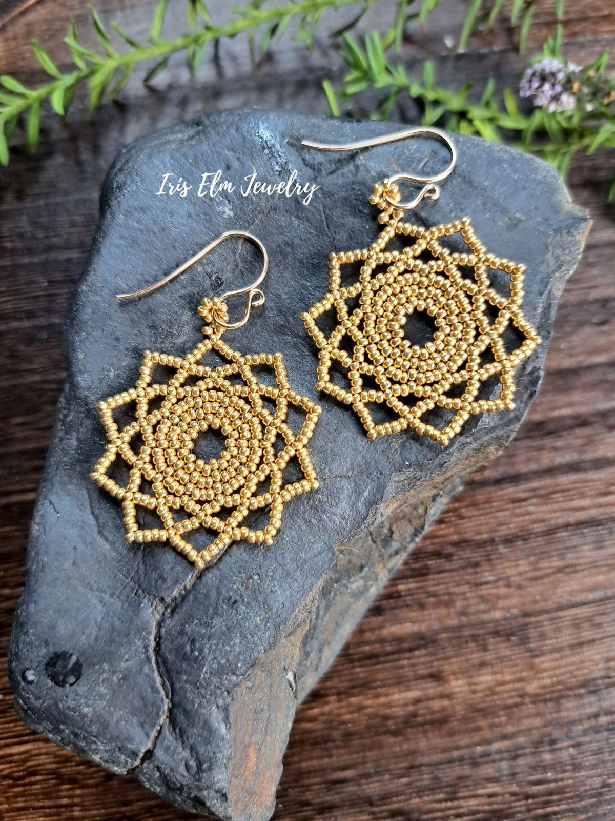 gold seed bead woven mandala handmade earrings by Iris Elm Jewelry on rocky surface