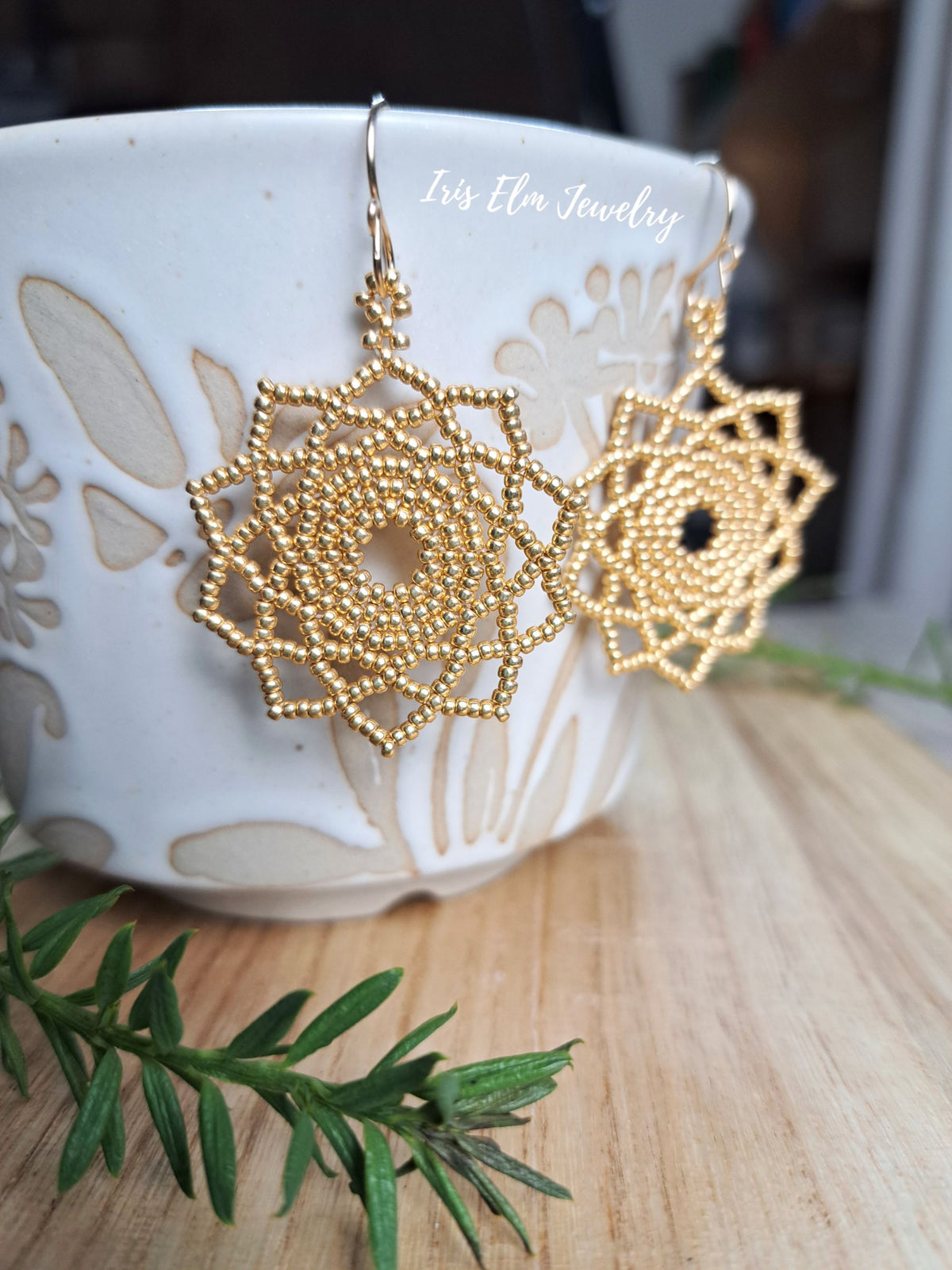 gold seed bead woven mandala handmade earrings by Iris Elm Jewelry on edge of ceramic pottery