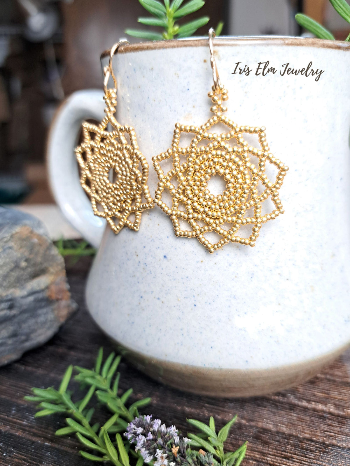gold seed bead woven mandala handmade earrings by Iris Elm Jewelry on edge of pottery