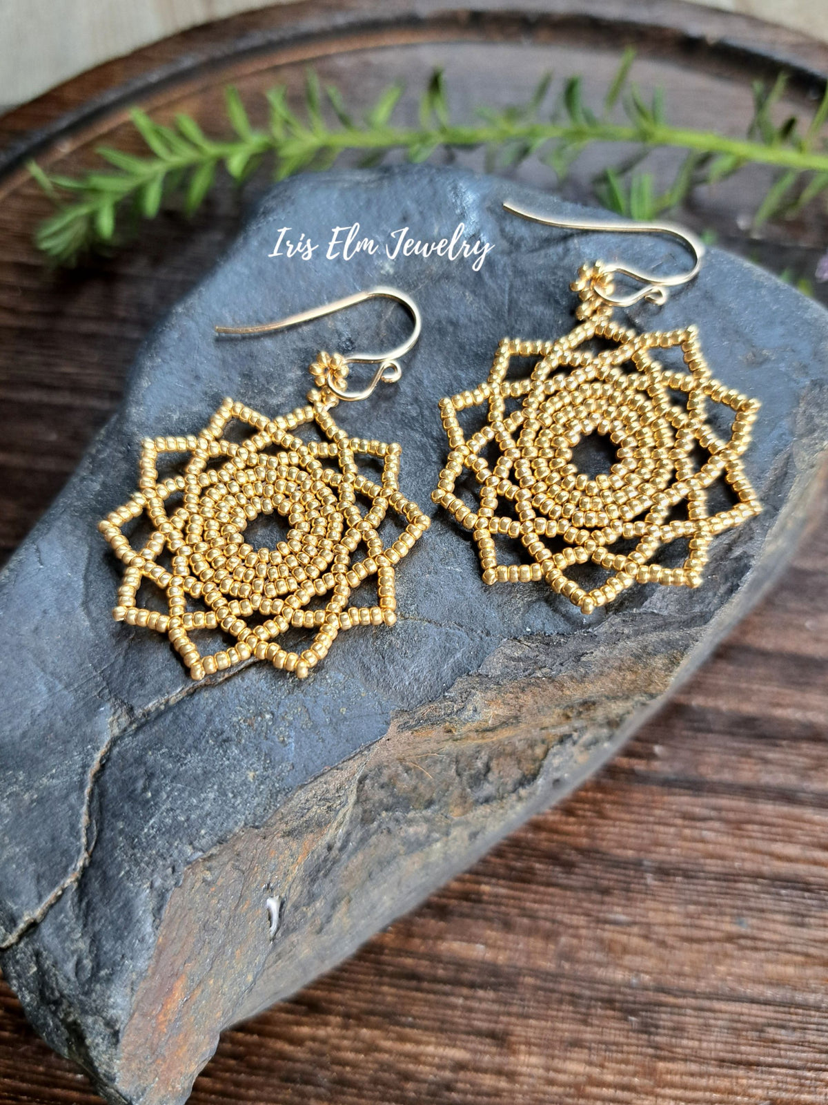 gold seed bead woven mandala handmade earrings by Iris Elm Jewelry on rocky surface