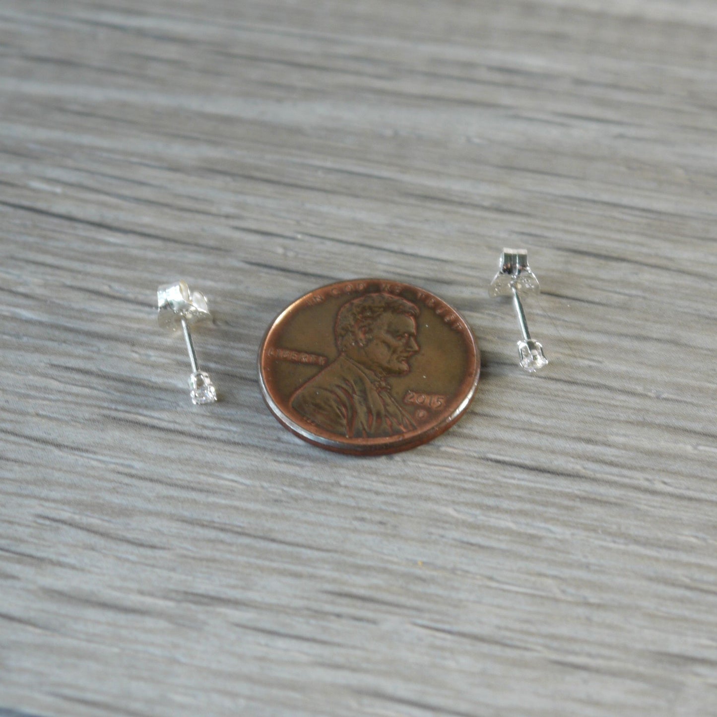 Small 2mm cubic zirconia silver earrings next to a penny on a wooden surface