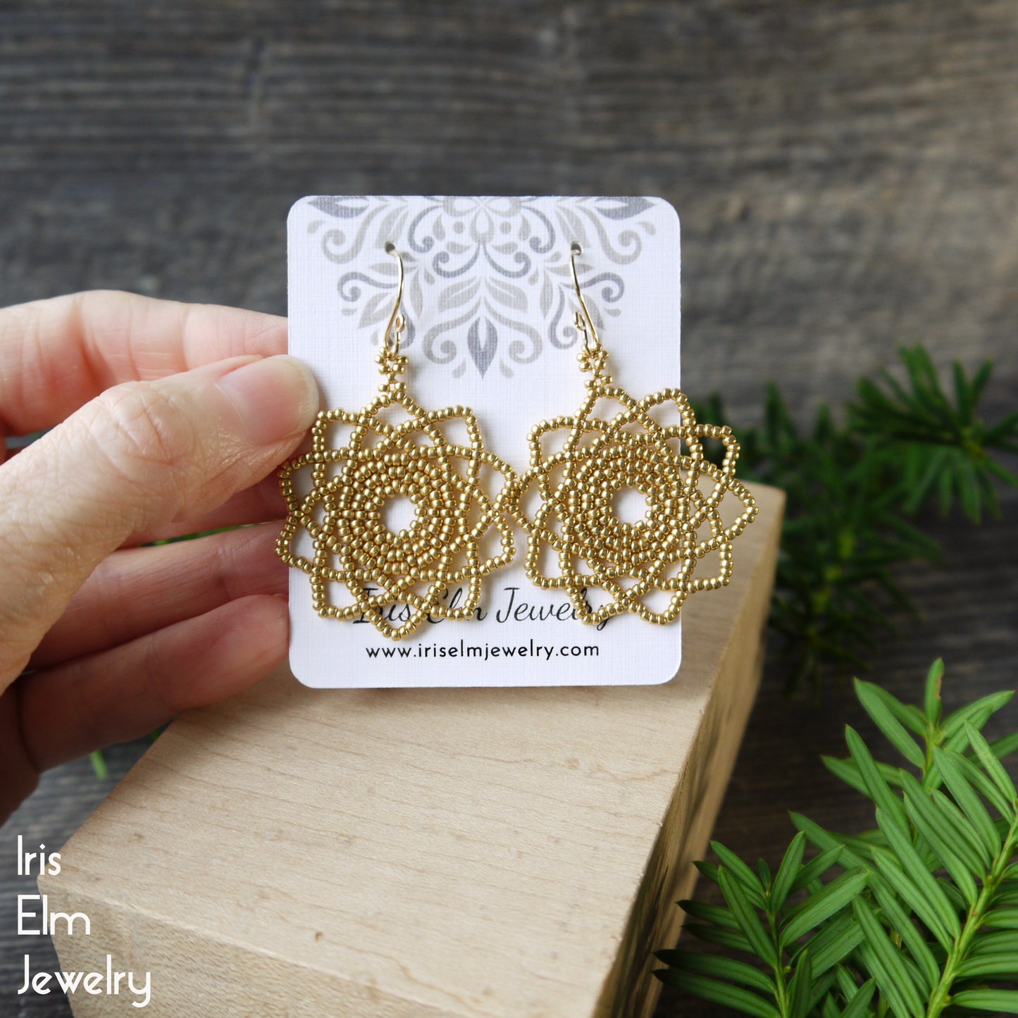 Gold seed bead mandala handcrafted earrings on a card held by a hand with a natural background
