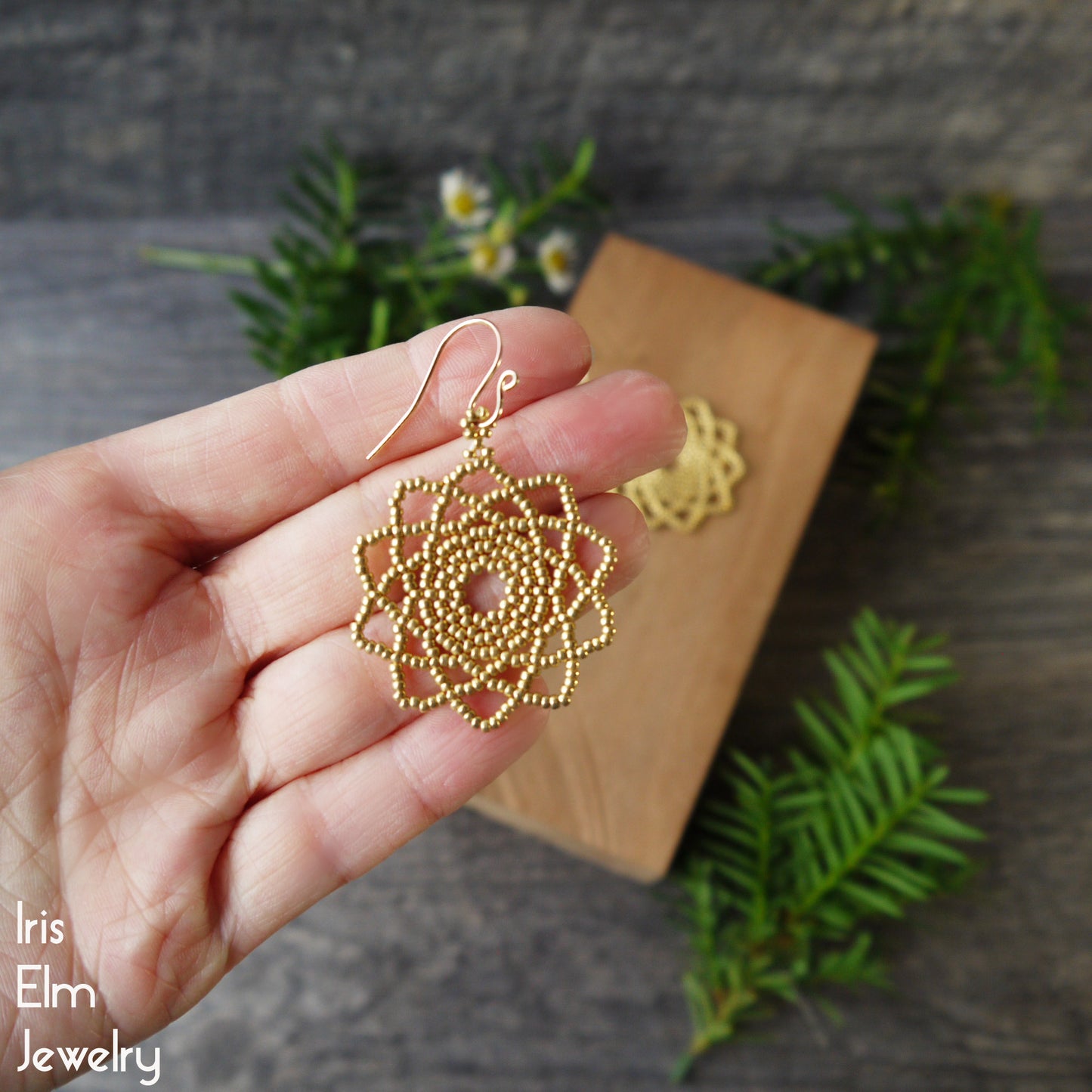 Gold glass seed bead woven mandala earrings held by a hand with a natural background