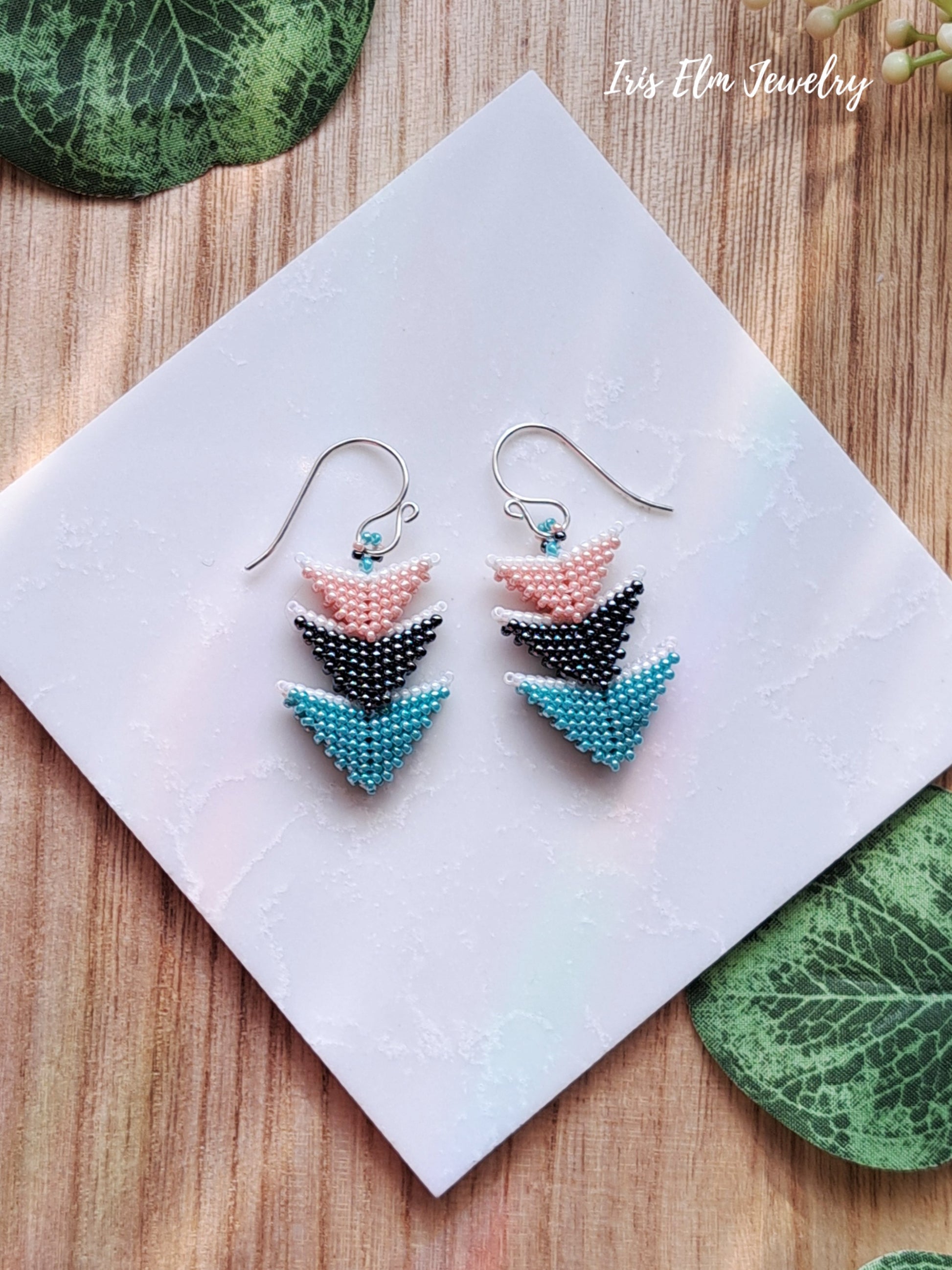 Colorful beaded arrow-shaped earrings on a white card with 'Iris Elm Jewelry' branding.