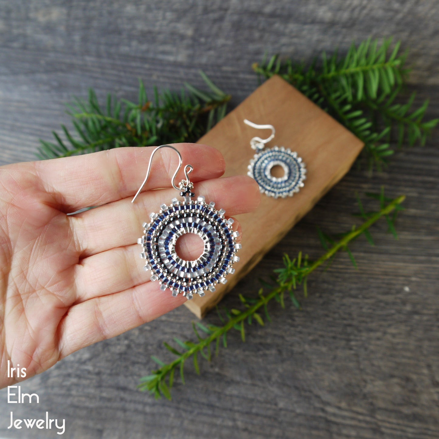Decorative beadwork blue seed bead hoop earrings held in a hand with a natural background