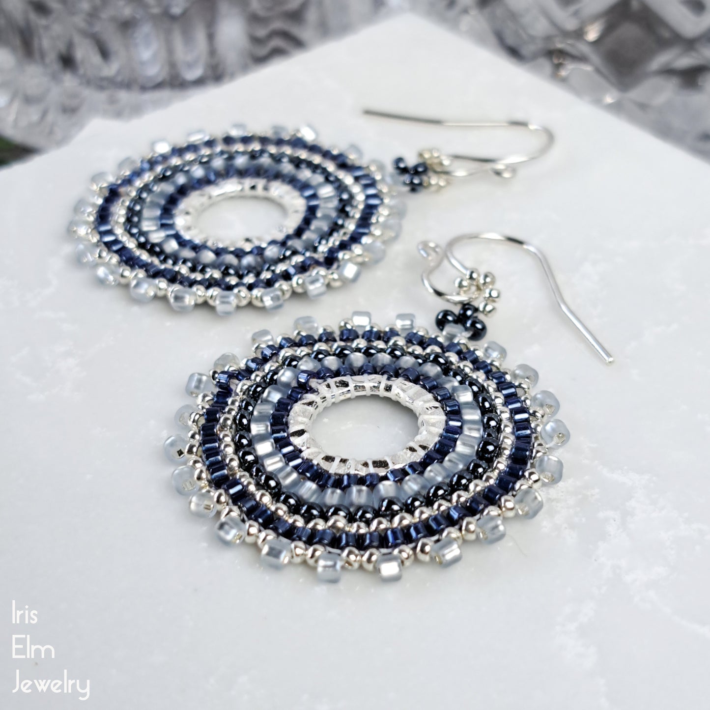 Beaded seed bead hoop handcrafted blue earrings on a white surface with 'Iris Elm Jewelry' branding.