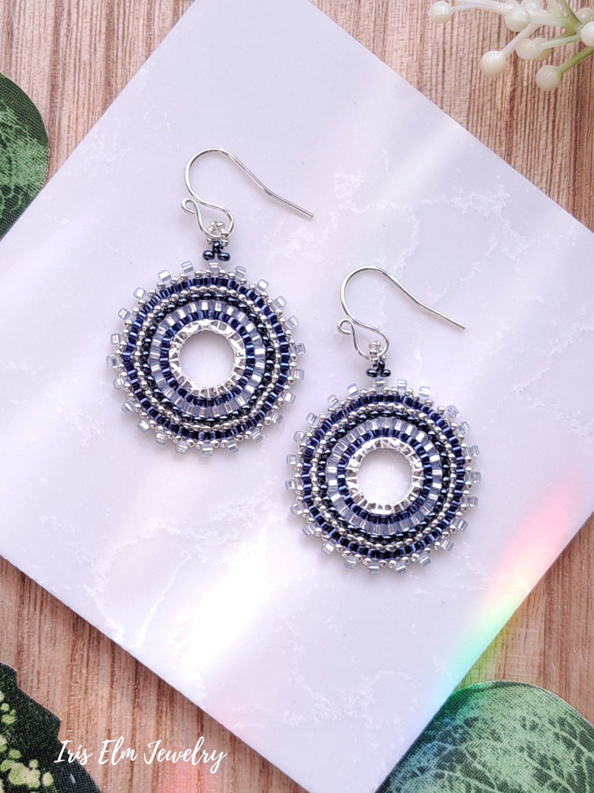 Pair of blue seed bead woven hoop beaded earrings on a white card with 'Iris Elm Jewelry' branding.