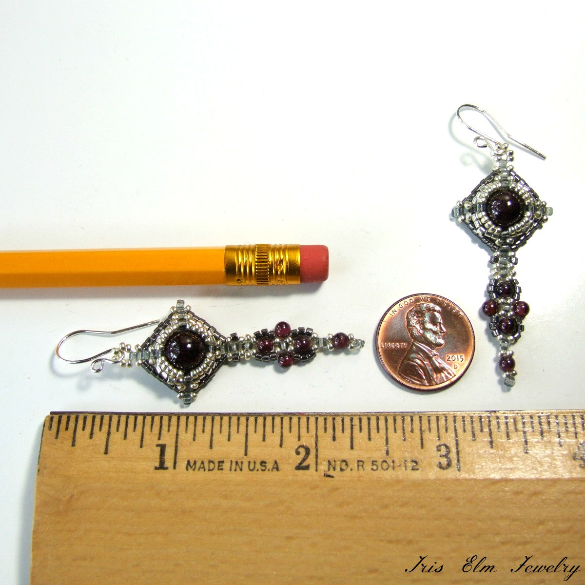 Pair of silver earrings with red gemstones next to a pencil and penny for scale on a white background.