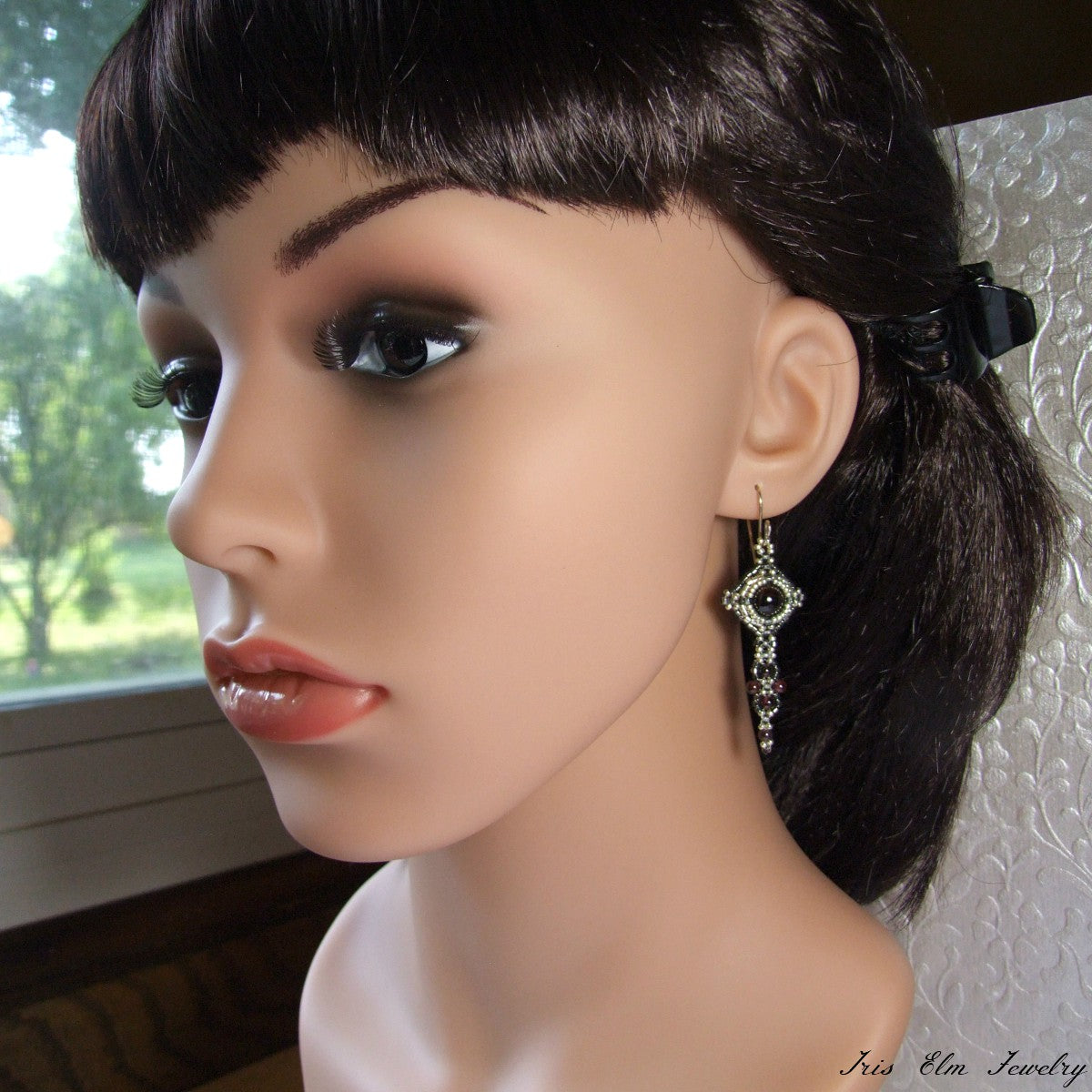 Mannequin head with dark hair and a red garnet earring, set against a neutral background.