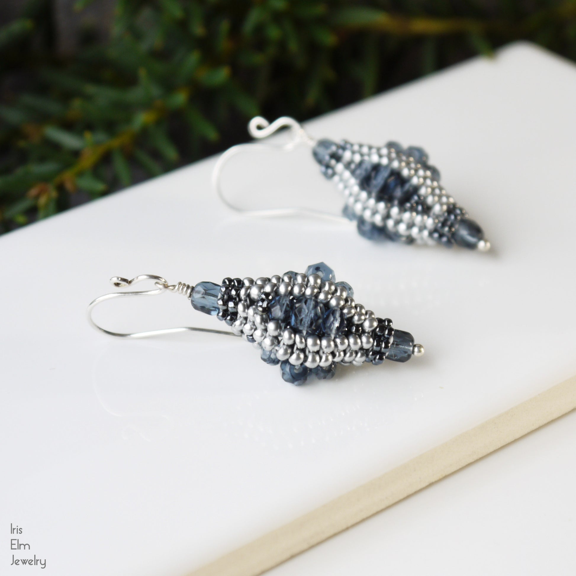 Pair of artisan handmade beaded blue glass earrings on a white surface with a blurred green background