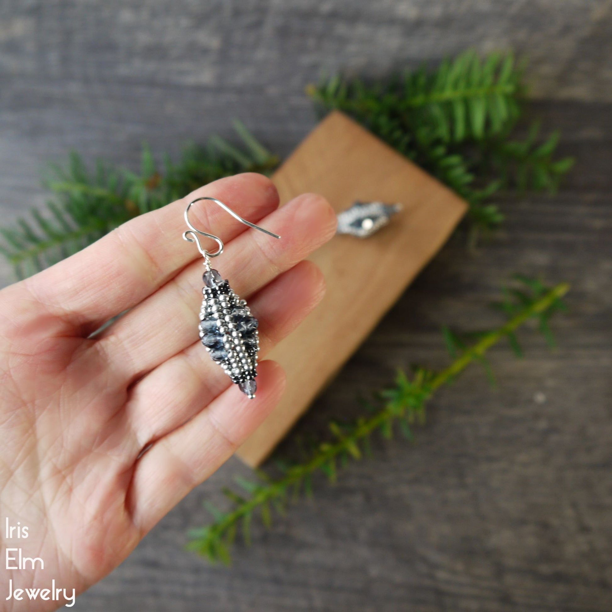 Silver and dusty blue lantern-shaped earring held by a hand with a natural background