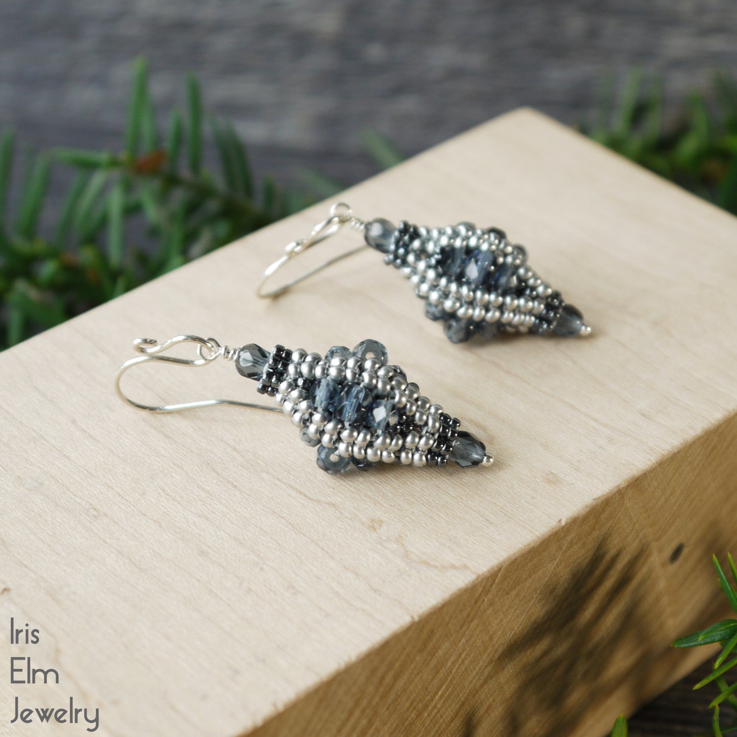 Pair of dusty blue handcrafted beaded earrings with intricate details on a wooden block with a natural background