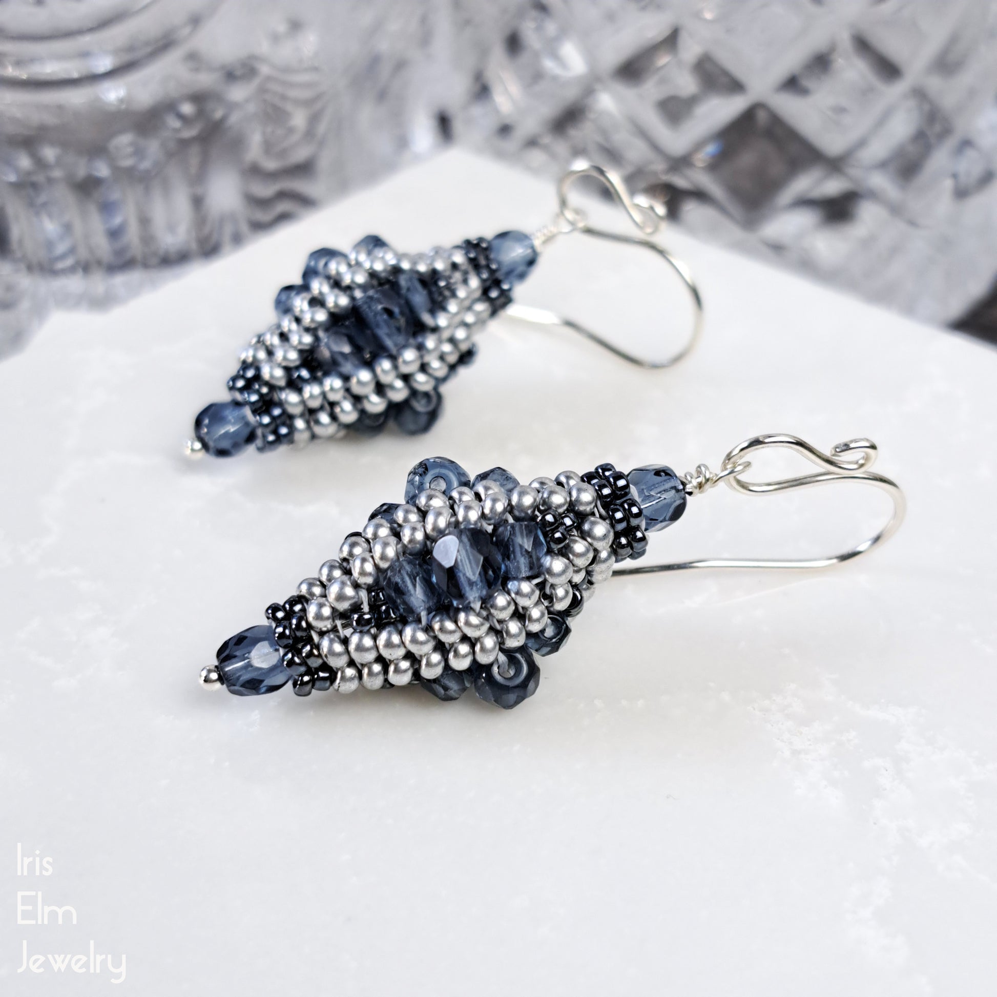 Beaded blue Czech glass lantern earrings on a white surface with a blurred background