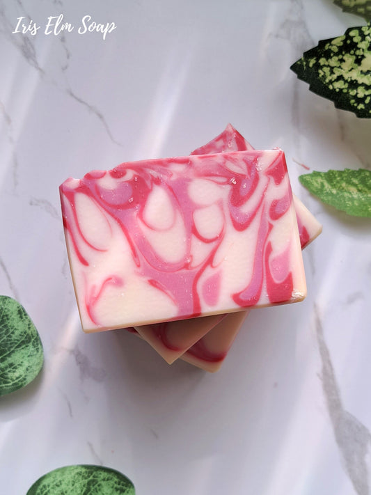 Pink and white swirled strawberry peach handmade soap bars on a marble surface with green leaves.