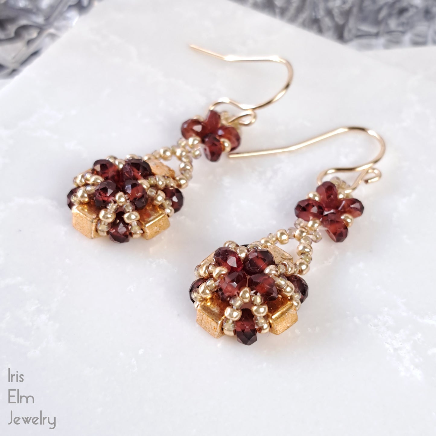 Gold glass and red garnet gemstone beaded earrings on a white surface with 'Iris Elm Jewelry' branding.