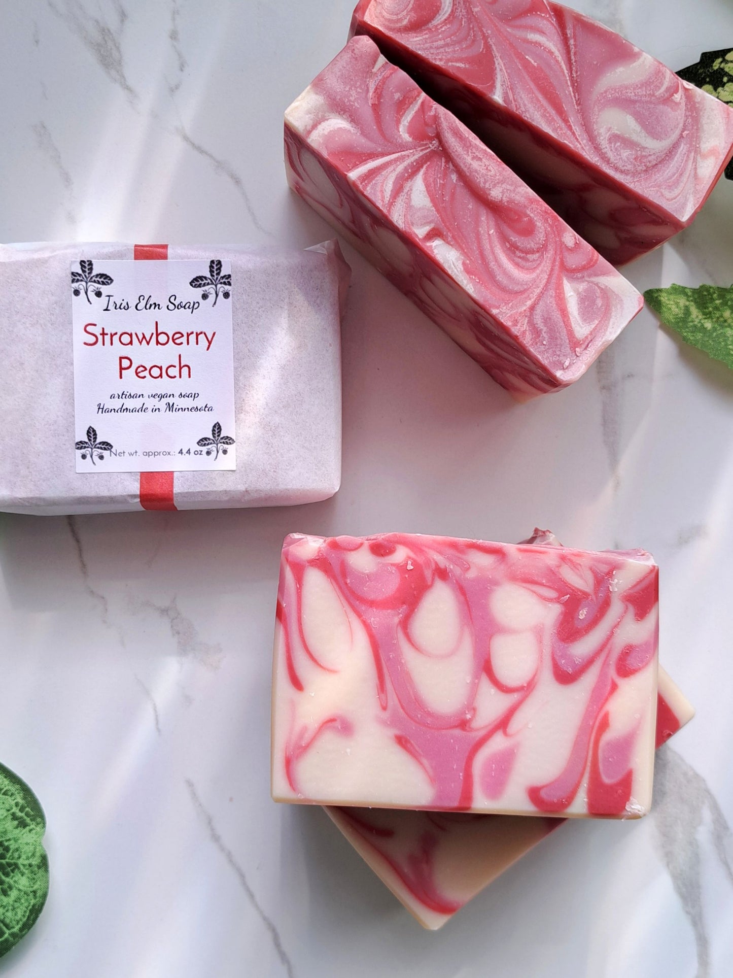 Two bars of strawberry peach soap with a packaging label on a marble surface.