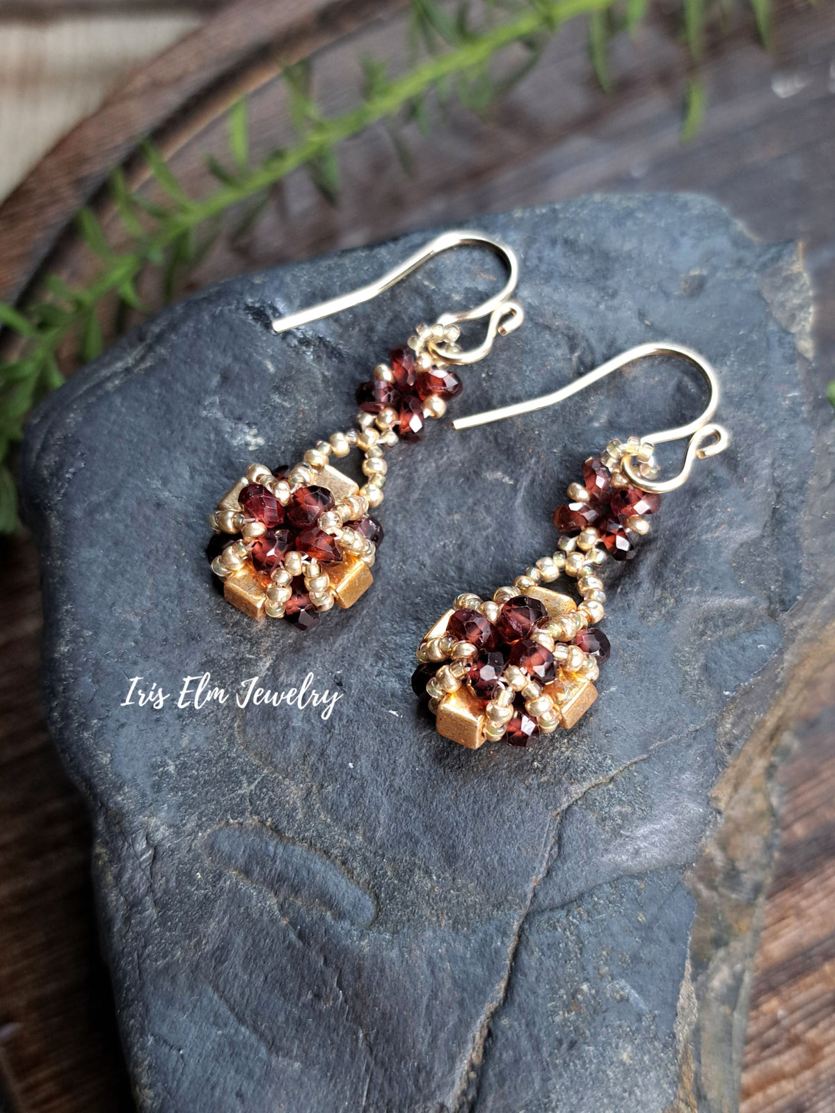 a pair of handmade red garnet gemstone and gold glass beaded earrings by Iris Elm Jewelry on rocky surface